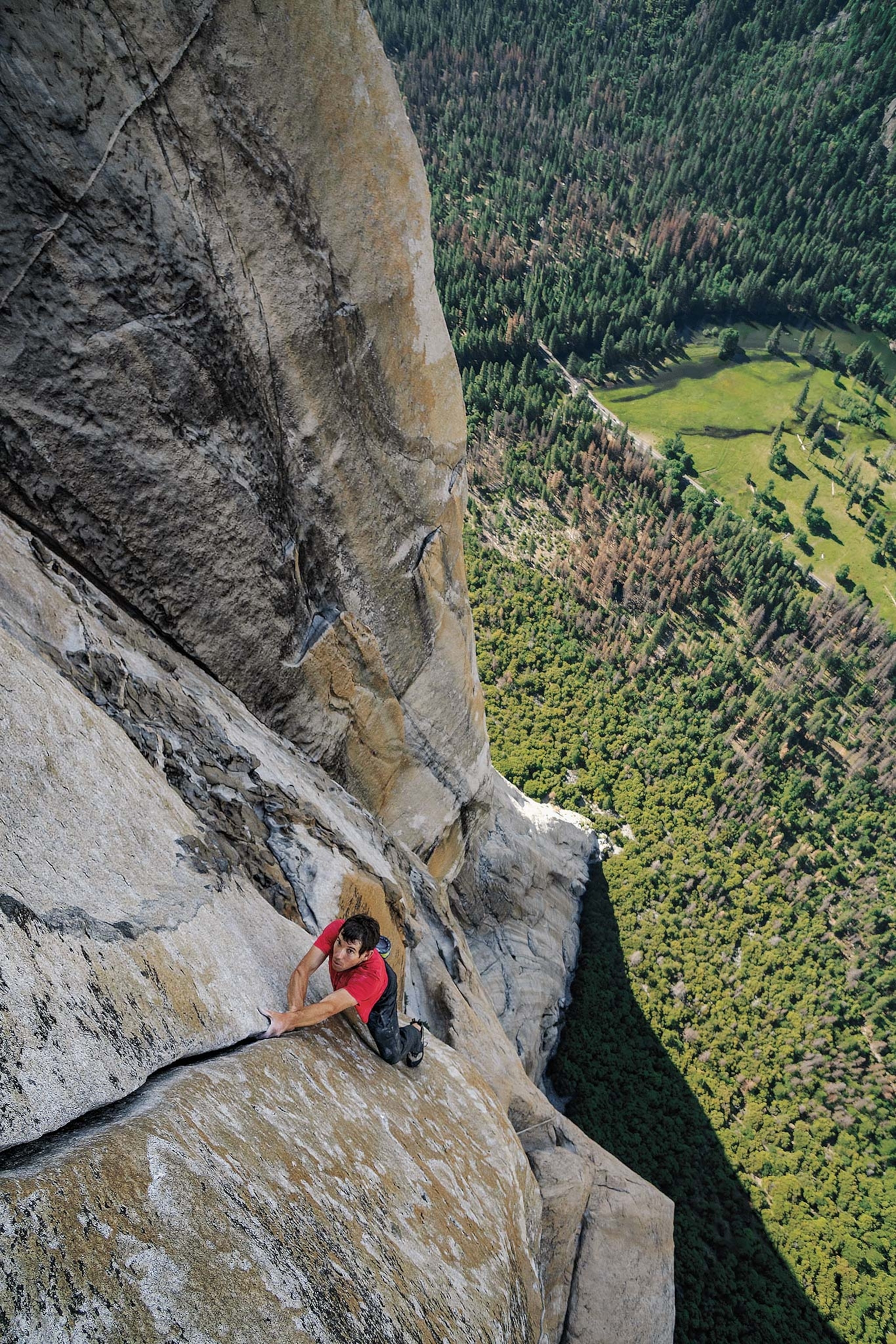 A top-down view of a man climbing cliffs without ropes or safety gear and the forest below