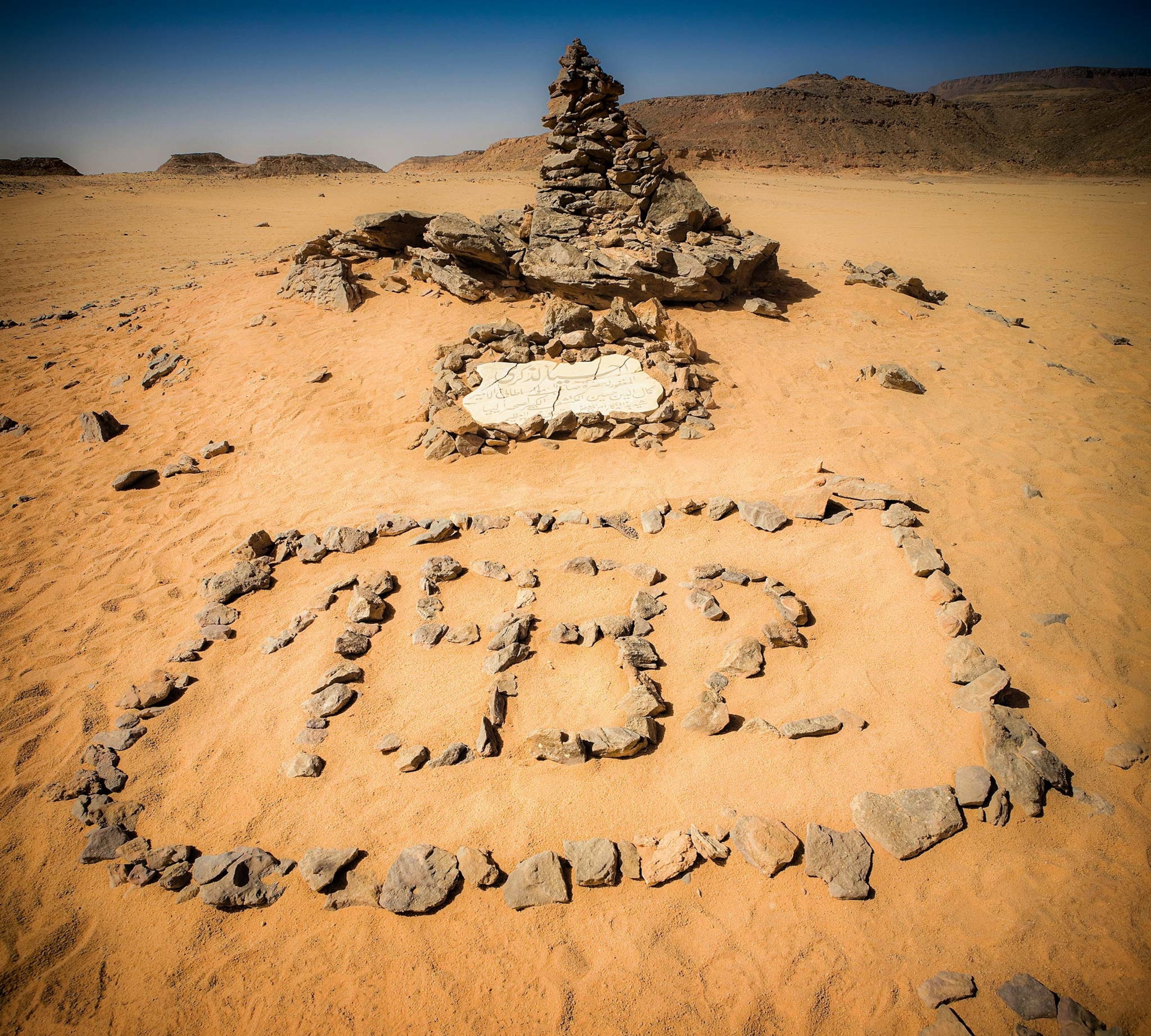 An angle of the white plague at the southern end of Gilk Kebir, with a rock pyramid formation behind it and 1932 written in stones in front