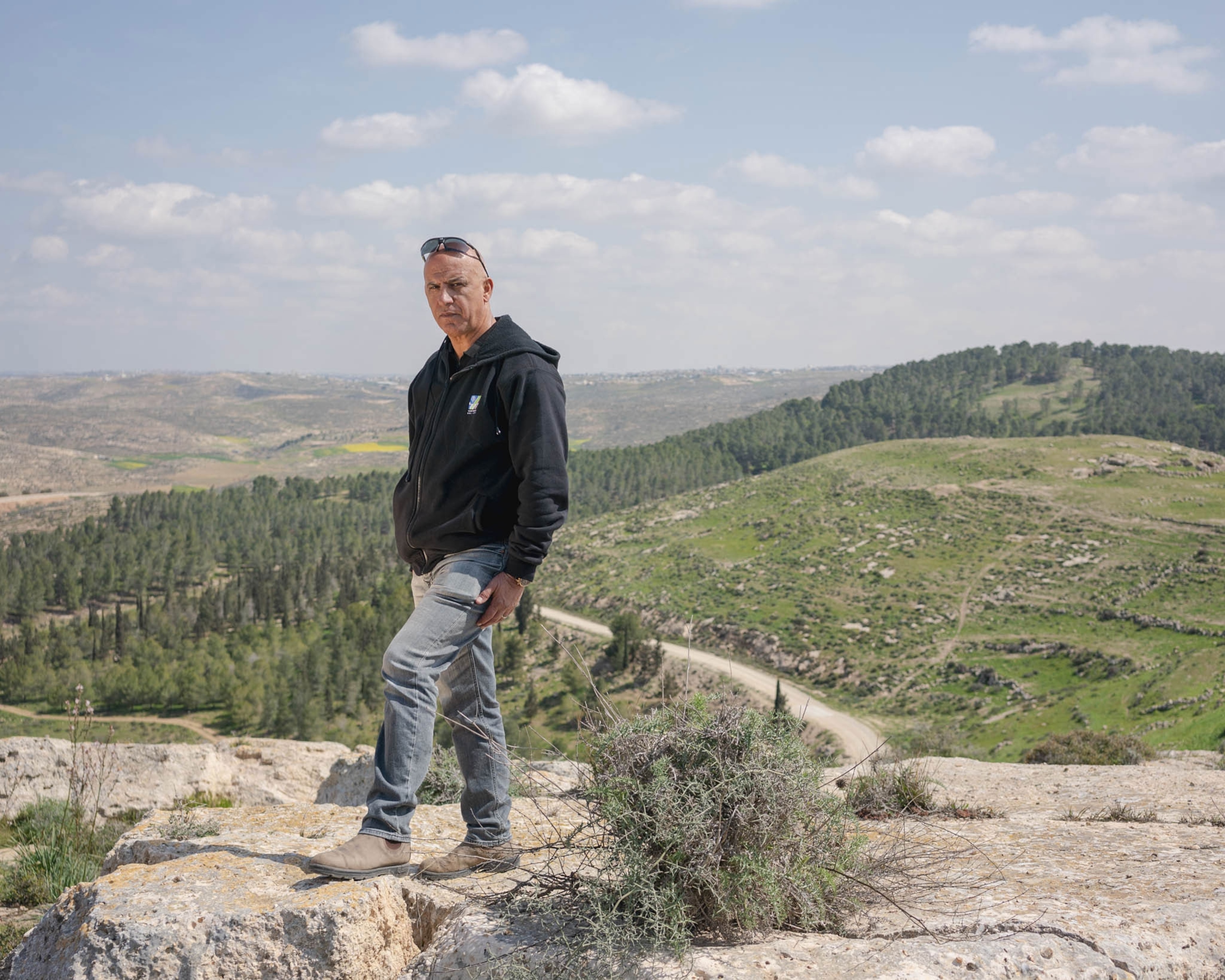 a man poses for a portrait at the top of a ridge line overlooking the forest