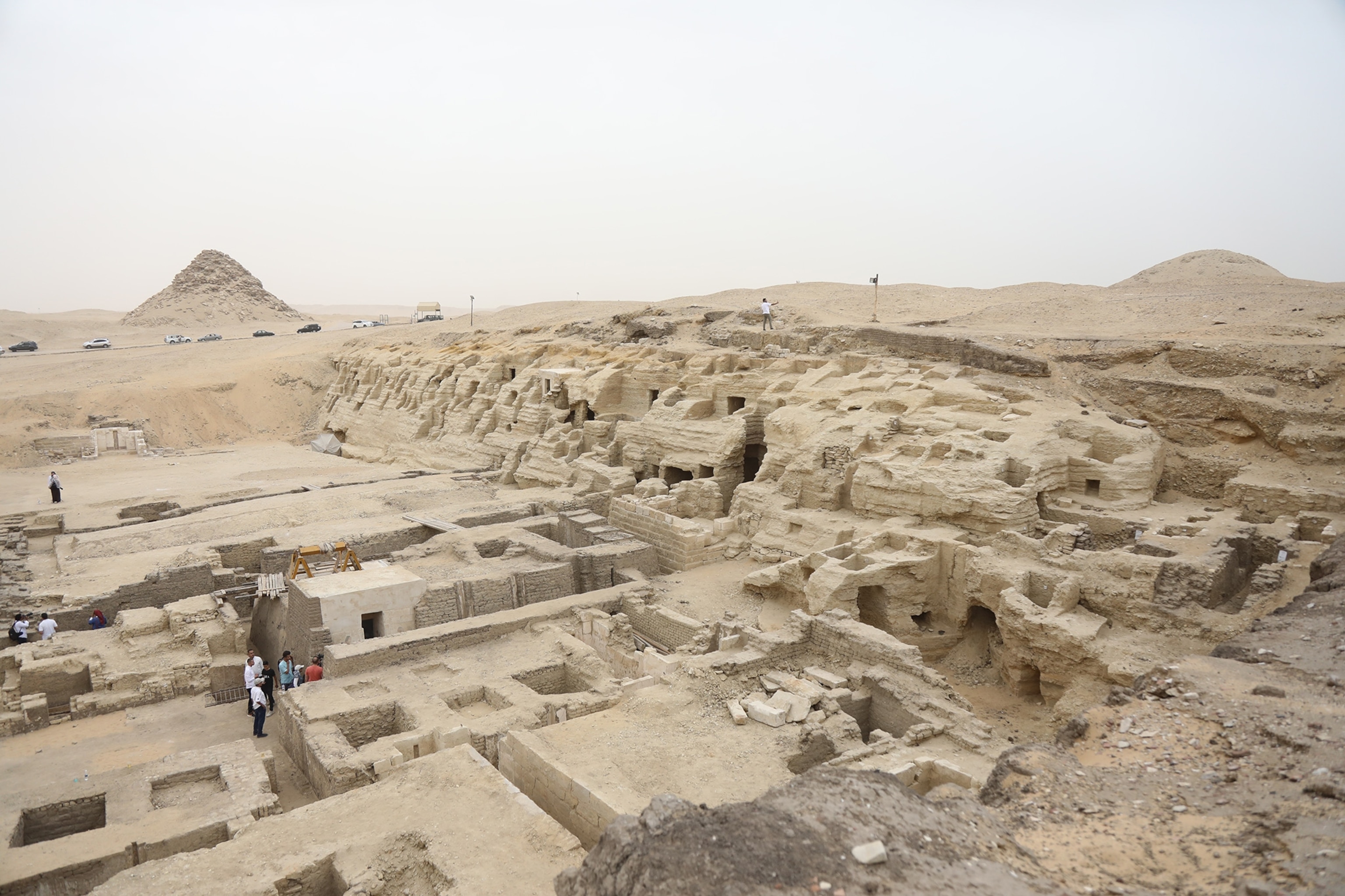 People visit archaeological excavation site with a pyramid in the background in the Saqqara region in Giza, Egypt.