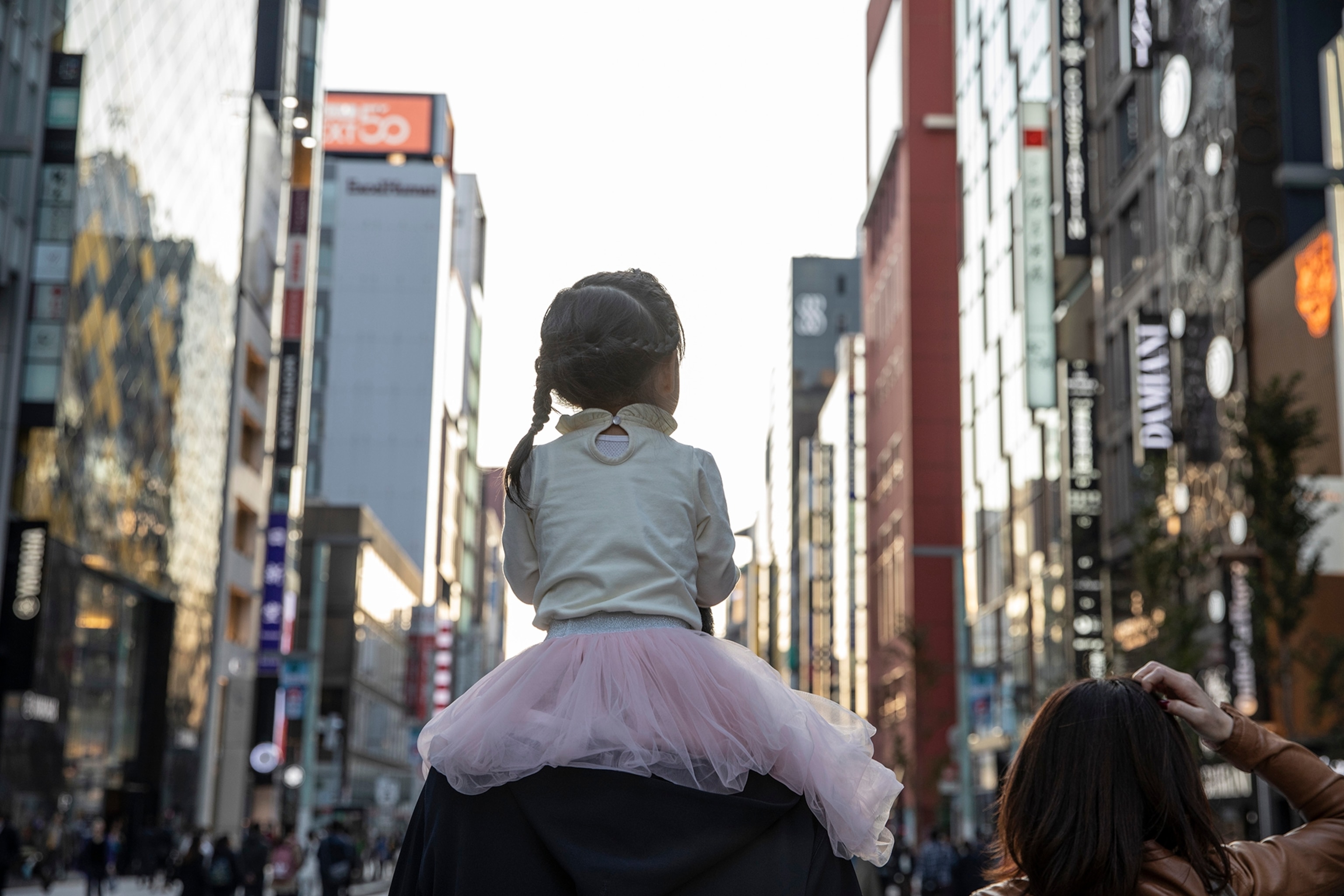 A young girl rides on the shoulders of an adult in the Ginza neighborhood in Tokyo, closed to traffic on a Saturday afternoon.