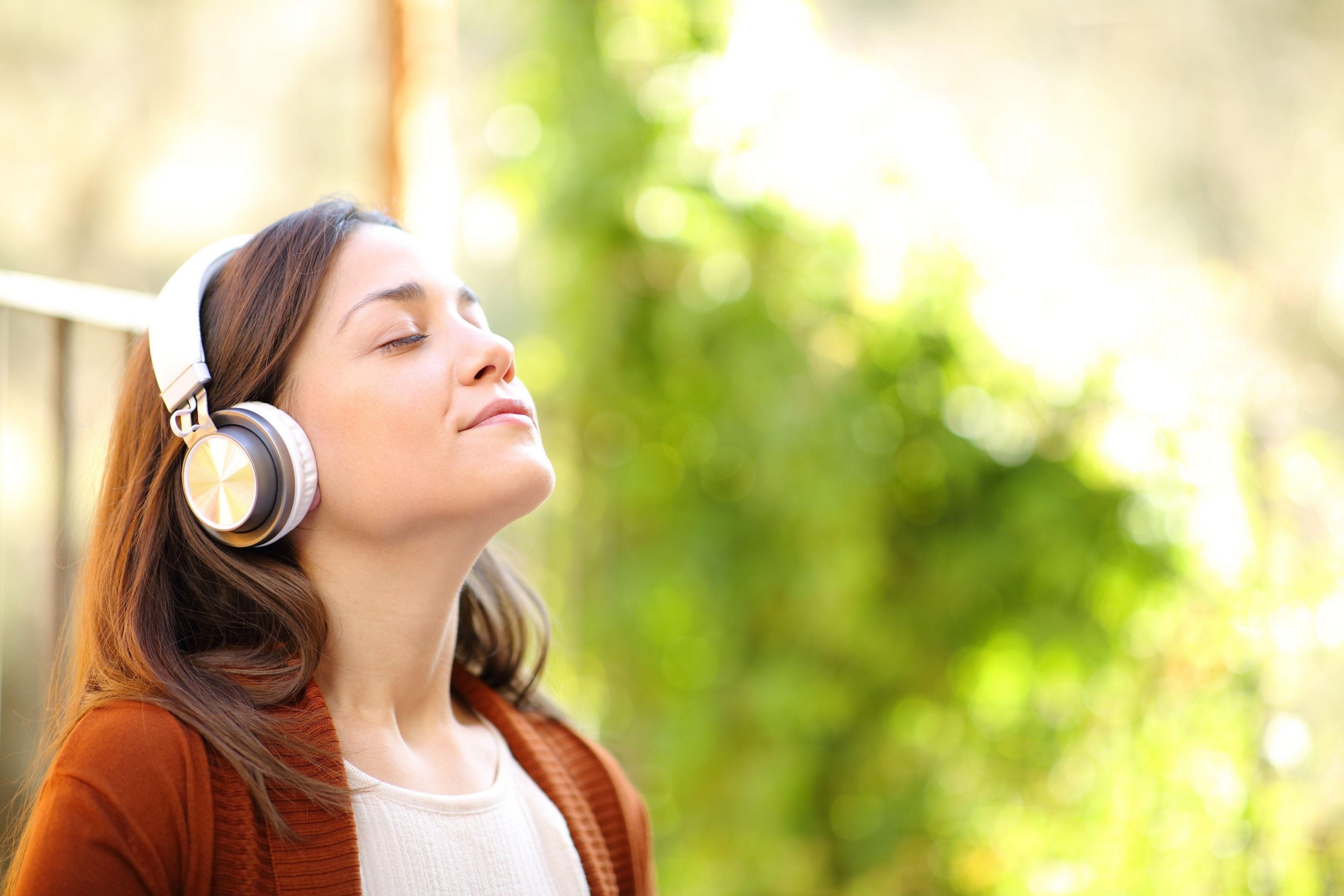 A young woman listens to relaxing audio through headphones outside on a sunny day