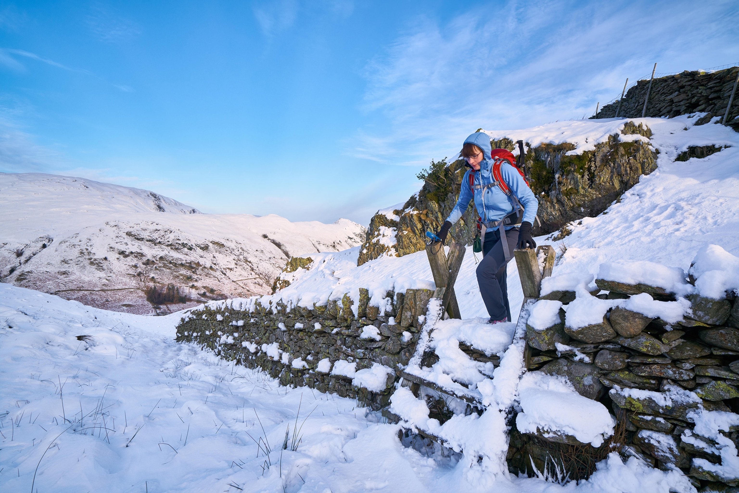 A hiker crossing a stile over a stone wall at Hartsop Above How in the English Lake District.