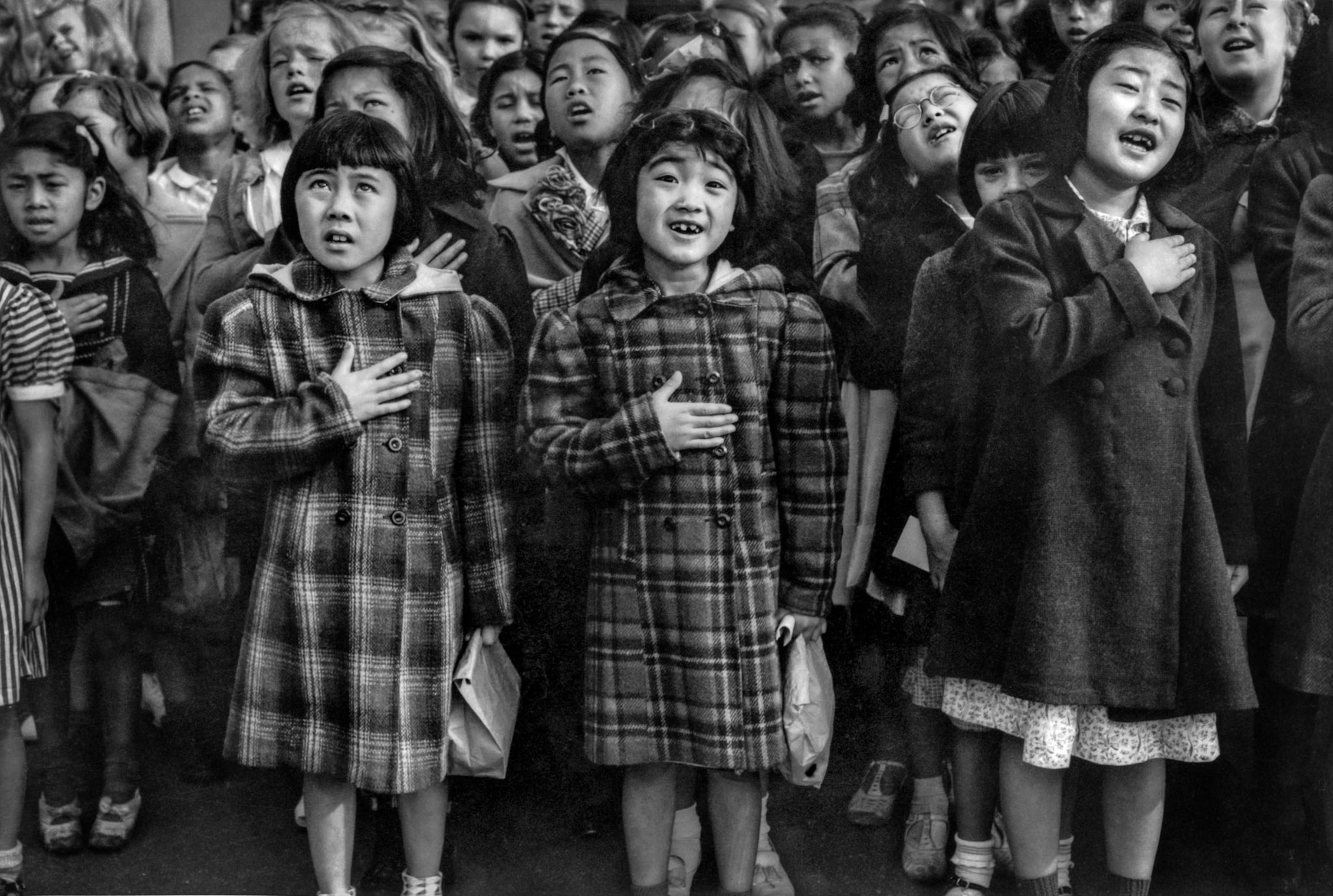 a group of young girls reciting a song with their right hand on their heart