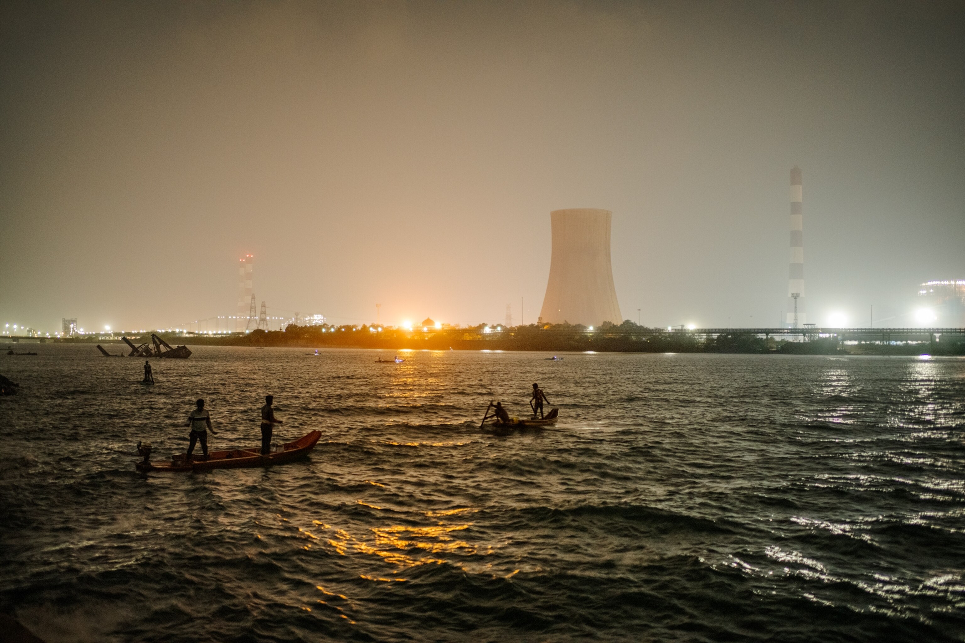 Picture of people fishing at night with the a thermal power plant in the background.