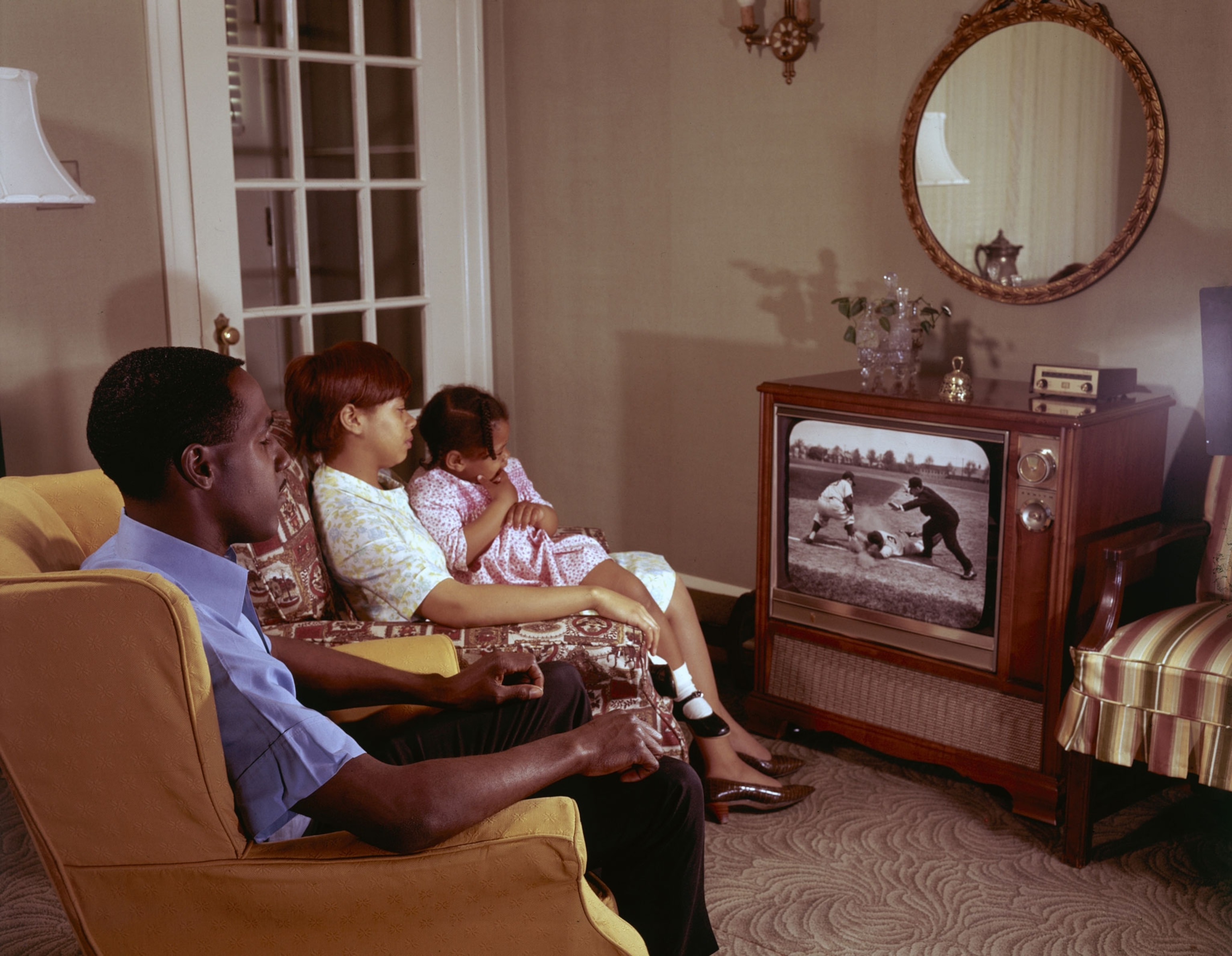a father, mother and child watch tv in a old fashioned livingroom