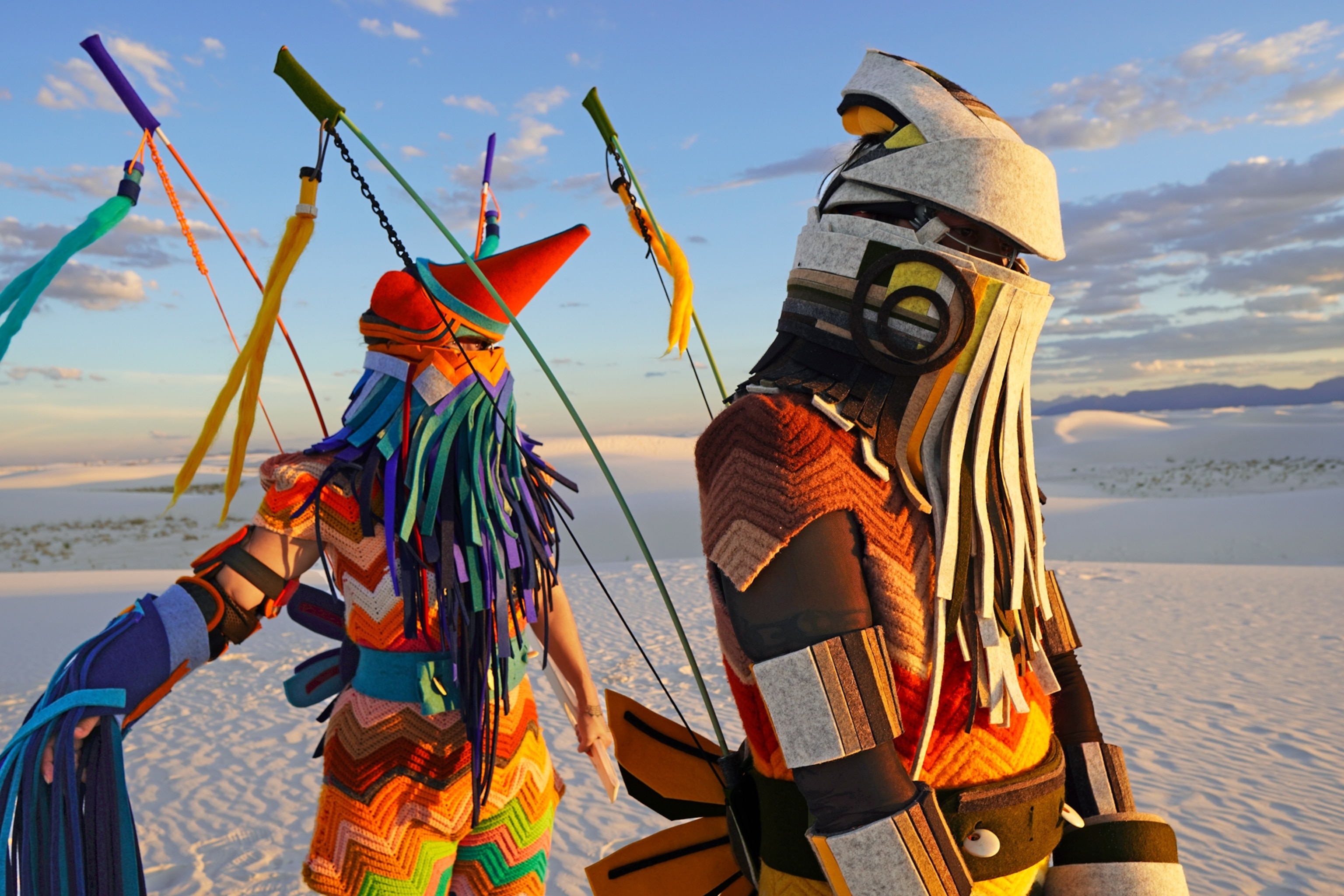 Two persons dressed in intricate combination of different kind of textile costumes, including felt and crochet in combination of solid colors.