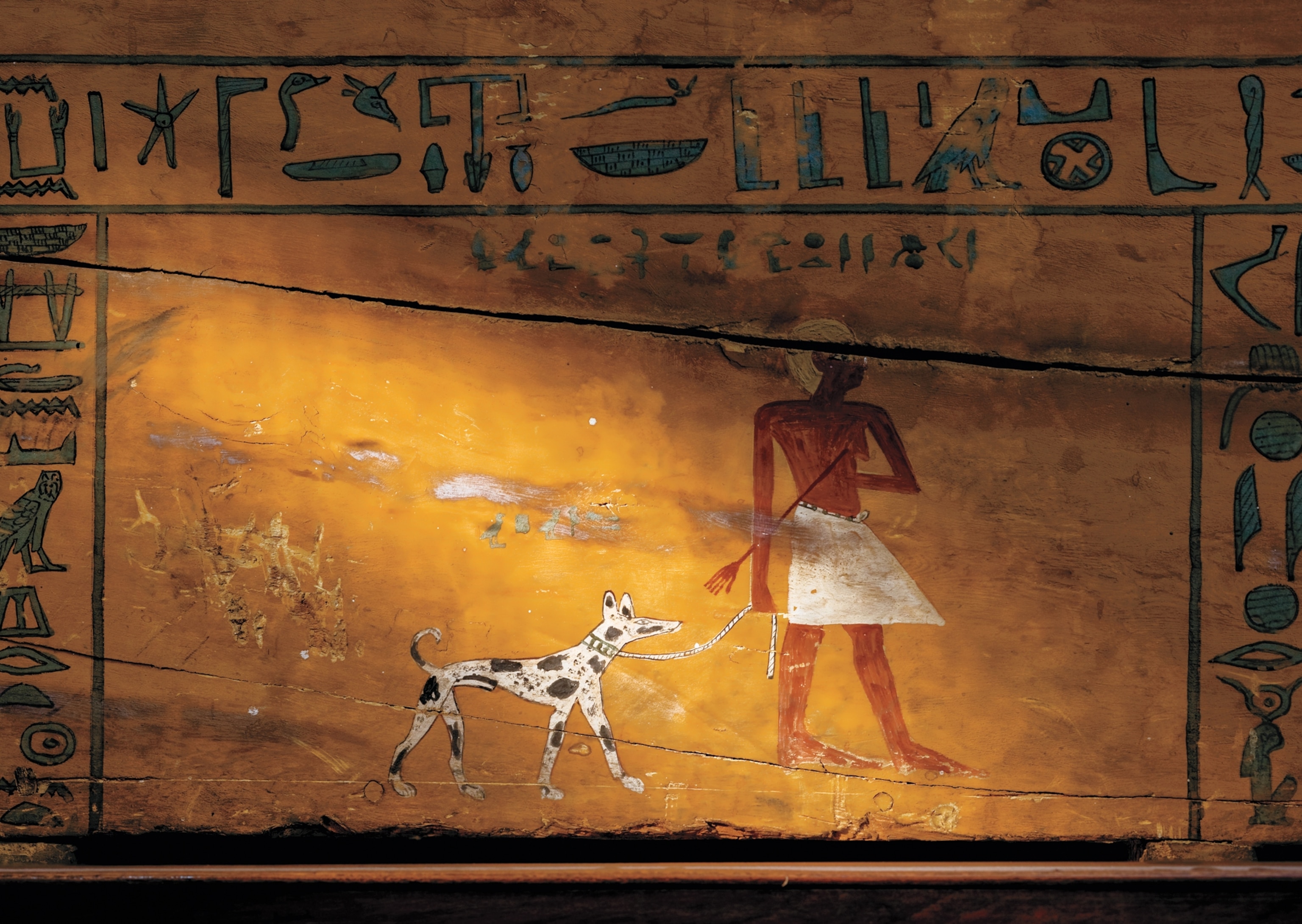 There is a drawing of a man leading his pet dog on a yellow worn-down surface. There are other symbols surrounding it. Light casts a shadow across this art.