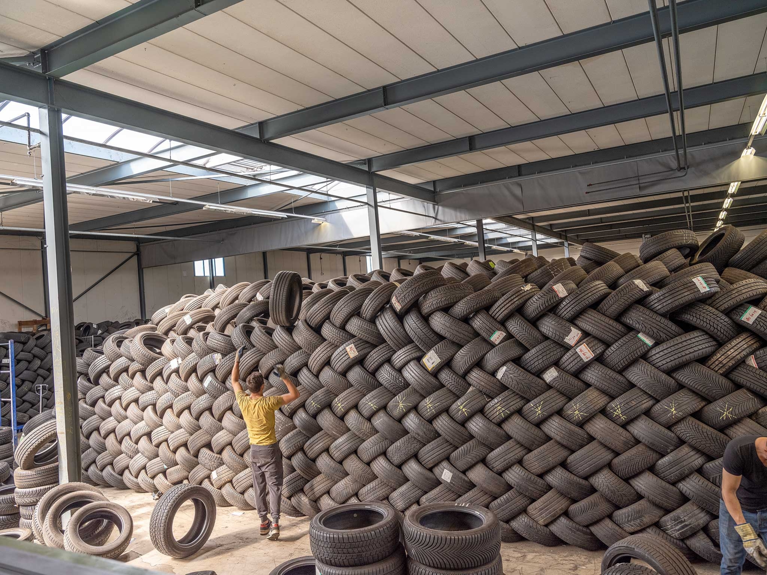 a man in a yellow shirt throwing a tire into a large neatly stacked pile of tires
