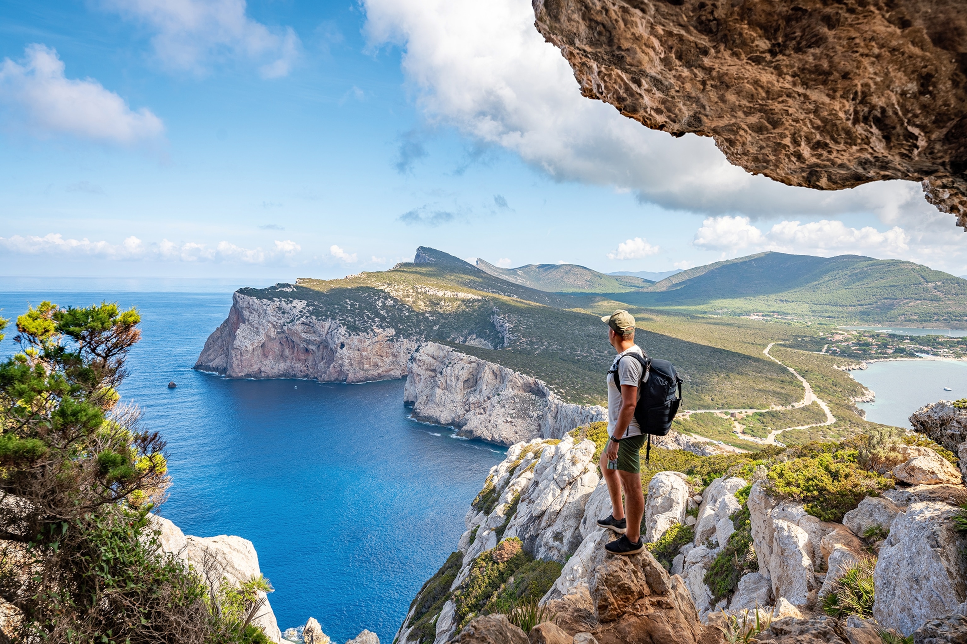 A man standing at the edge of an overhung cliff looking out on the seaside cliff coastline ahead.