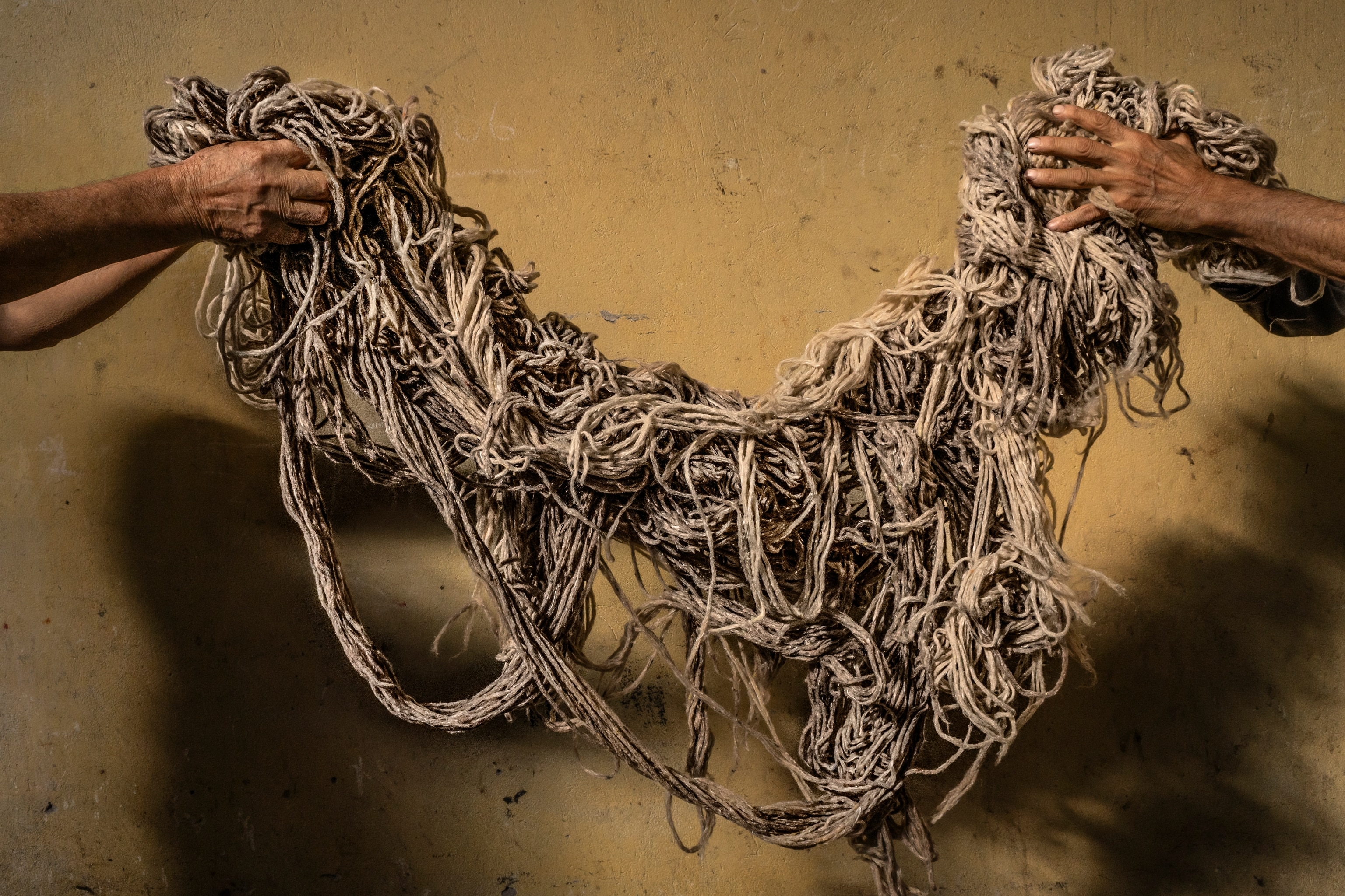 Two people are holding up a tangle of yarn across the frame