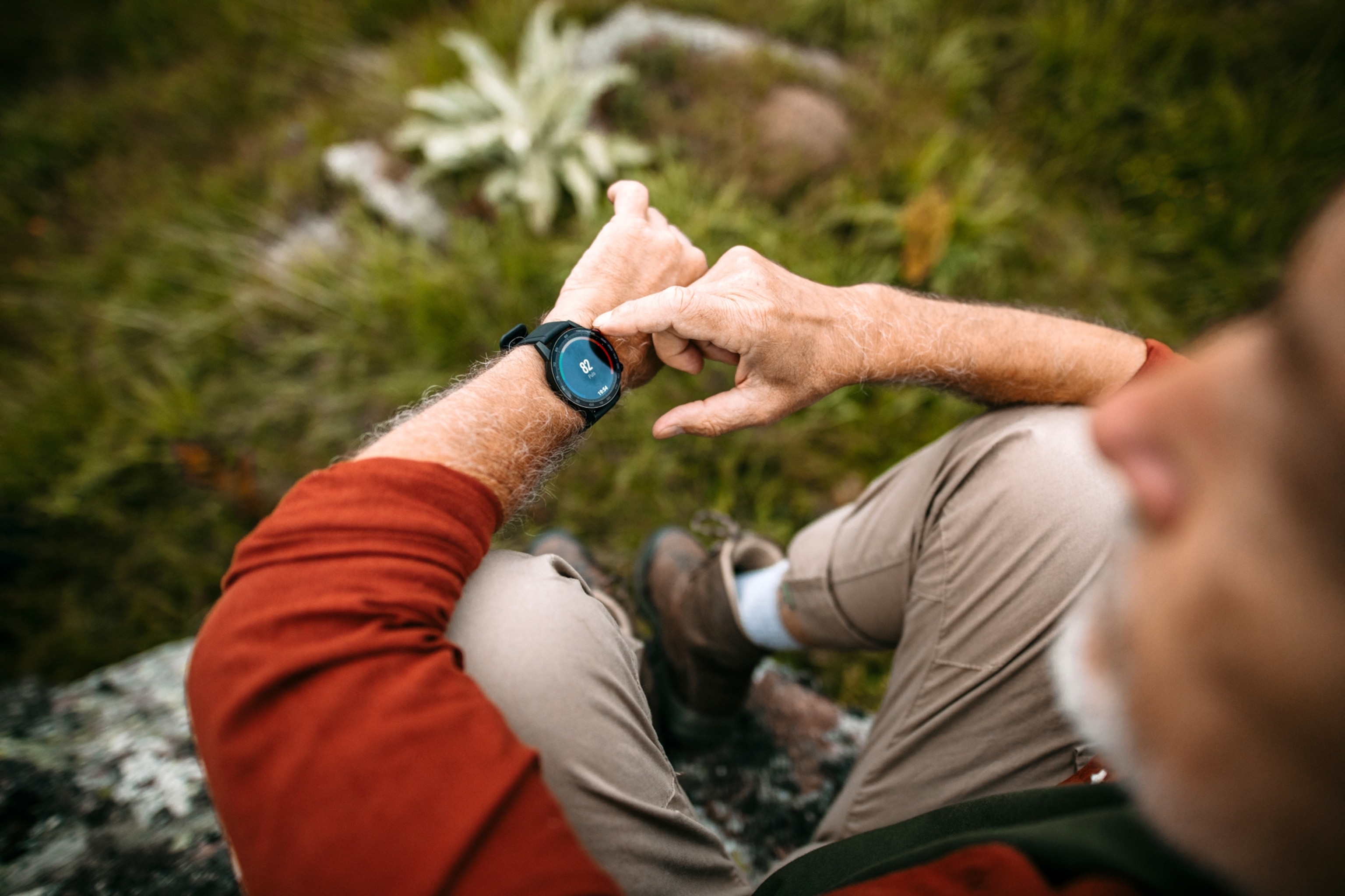 An overhead view of a senior man checking his fitness watch as he sits on a boulder.
