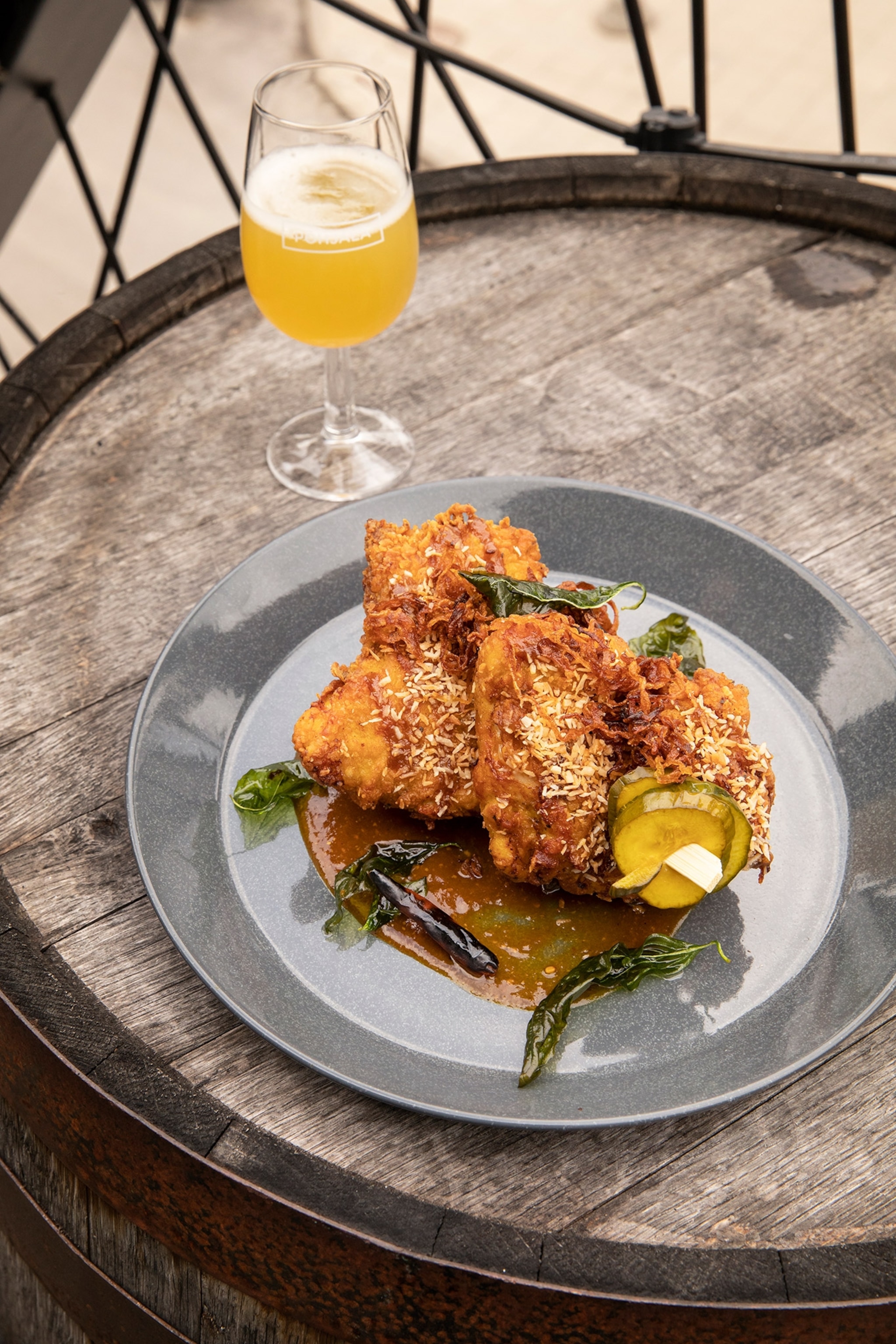 A plate of crispy chicken on a barrel and a glass of beer.