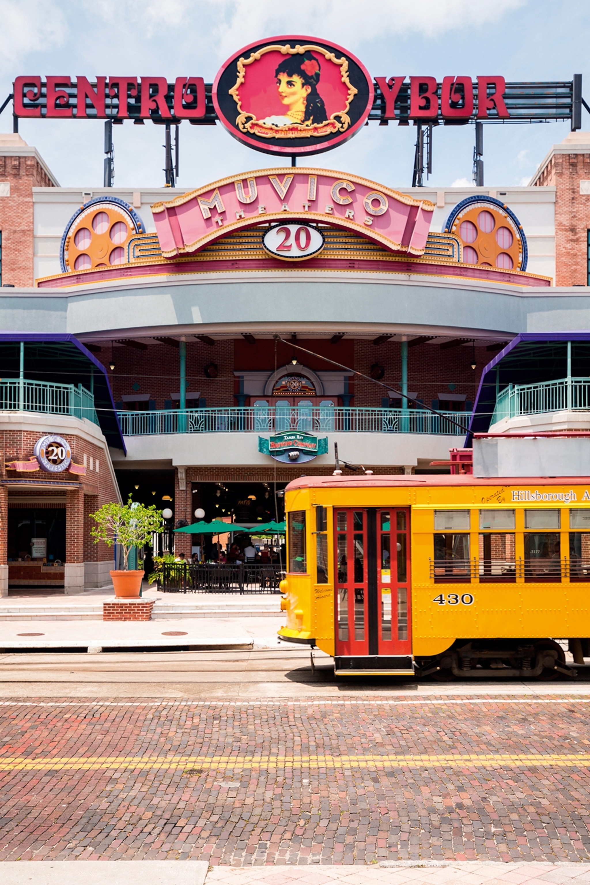 The exterior of a colourful remodeled cigar warehouse with kitsch signs and a tram passing by in front.