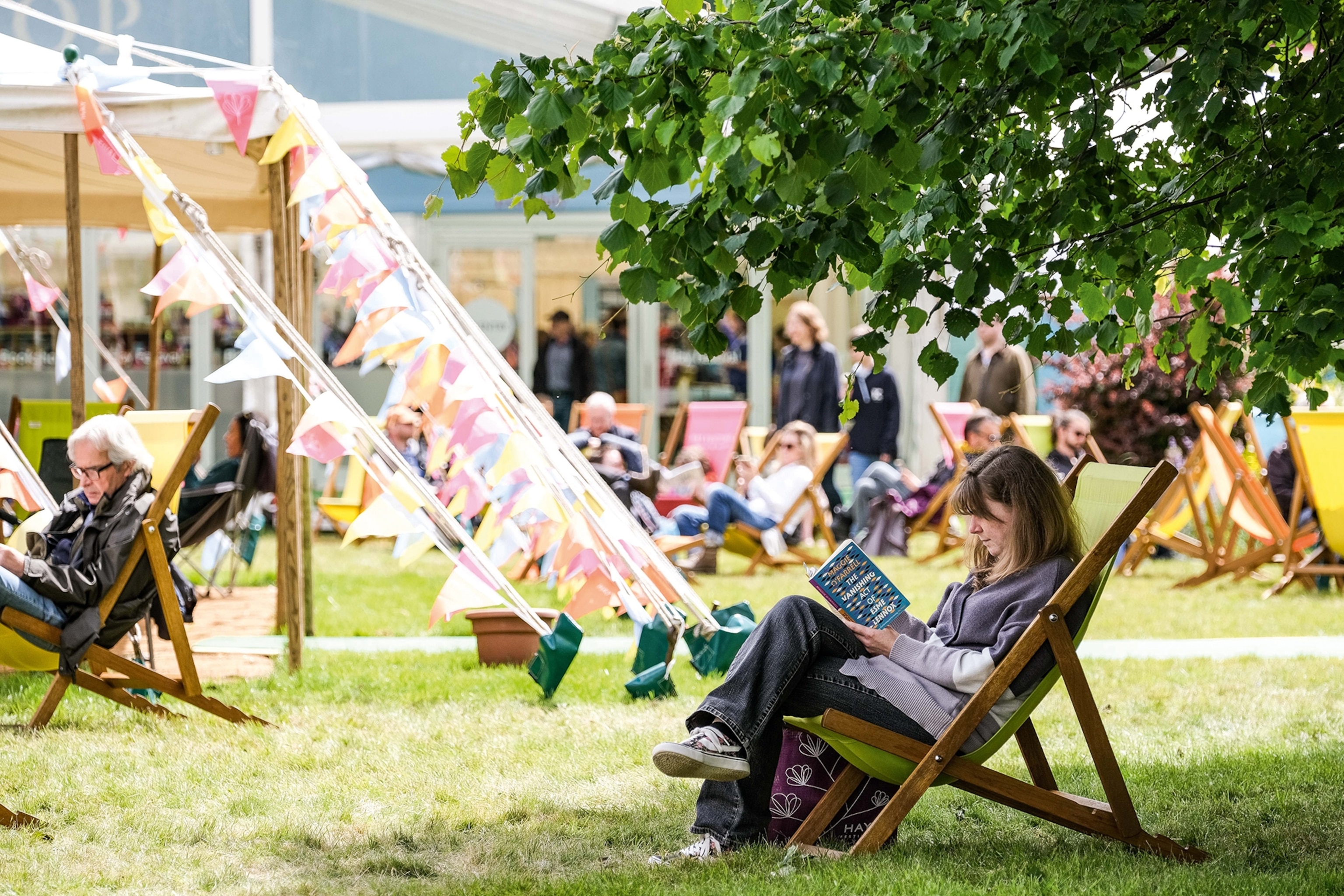 Woman reading a book in a deck chair under a tree at The Hay Festival.