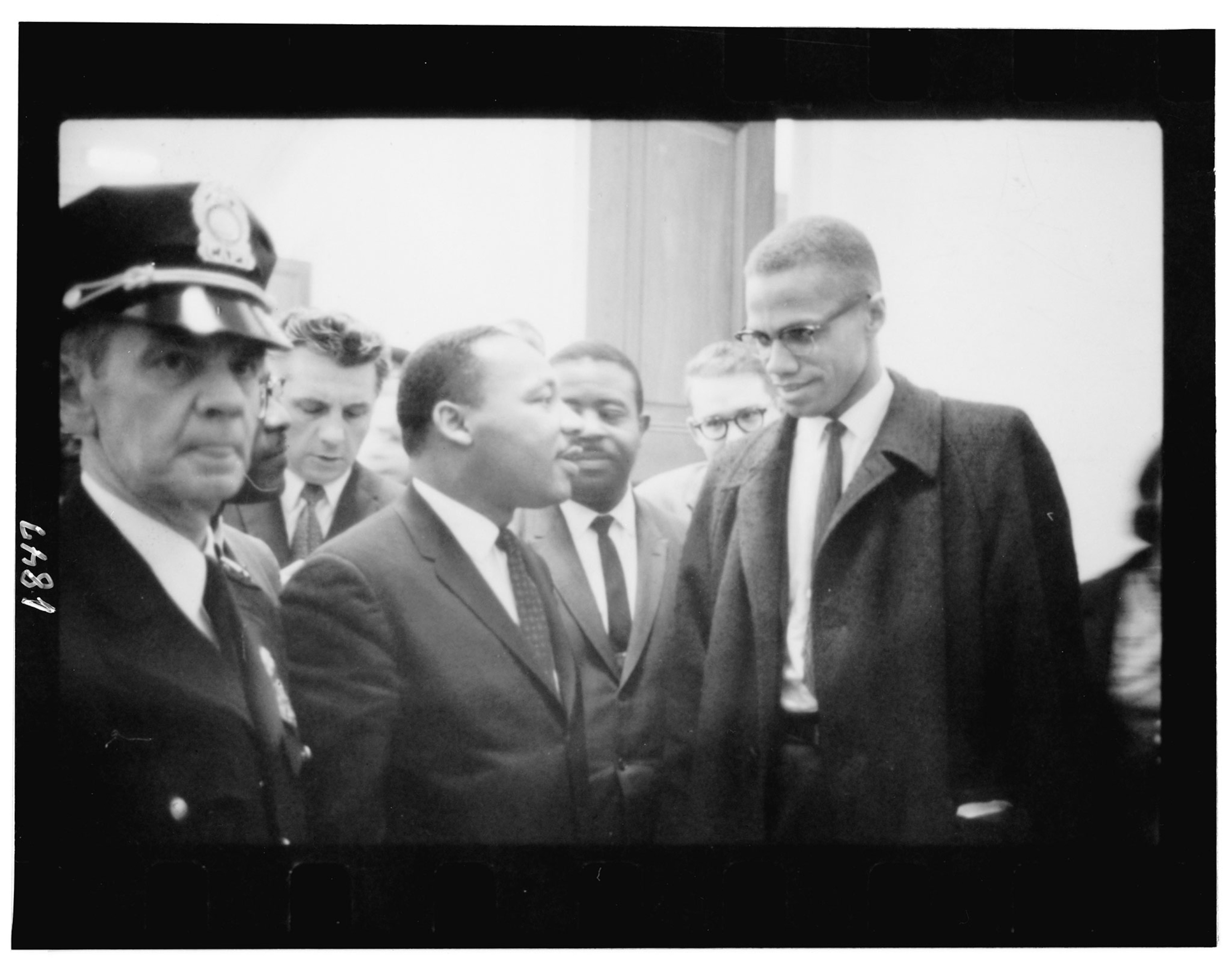 Martin Luther King and Malcolm X after King's press conference at the U.S. Capitol about the Senate debate on the Civil Rights Act of 1964. A police offer is seen in the foreground to the left of Martin Luther King and other men are in the background.