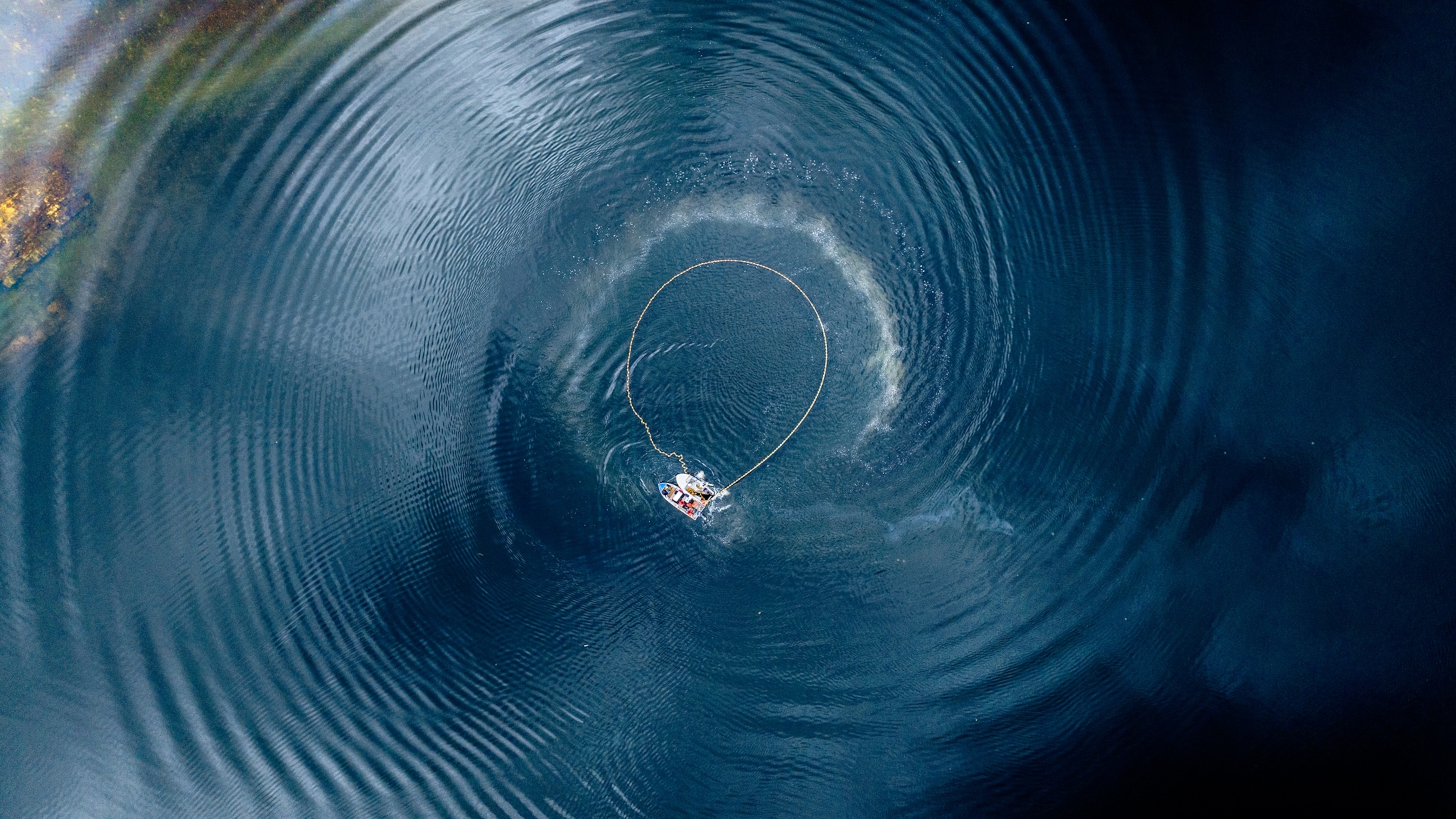 An aerial shot of a fishing boat with a large rope cast in a circle