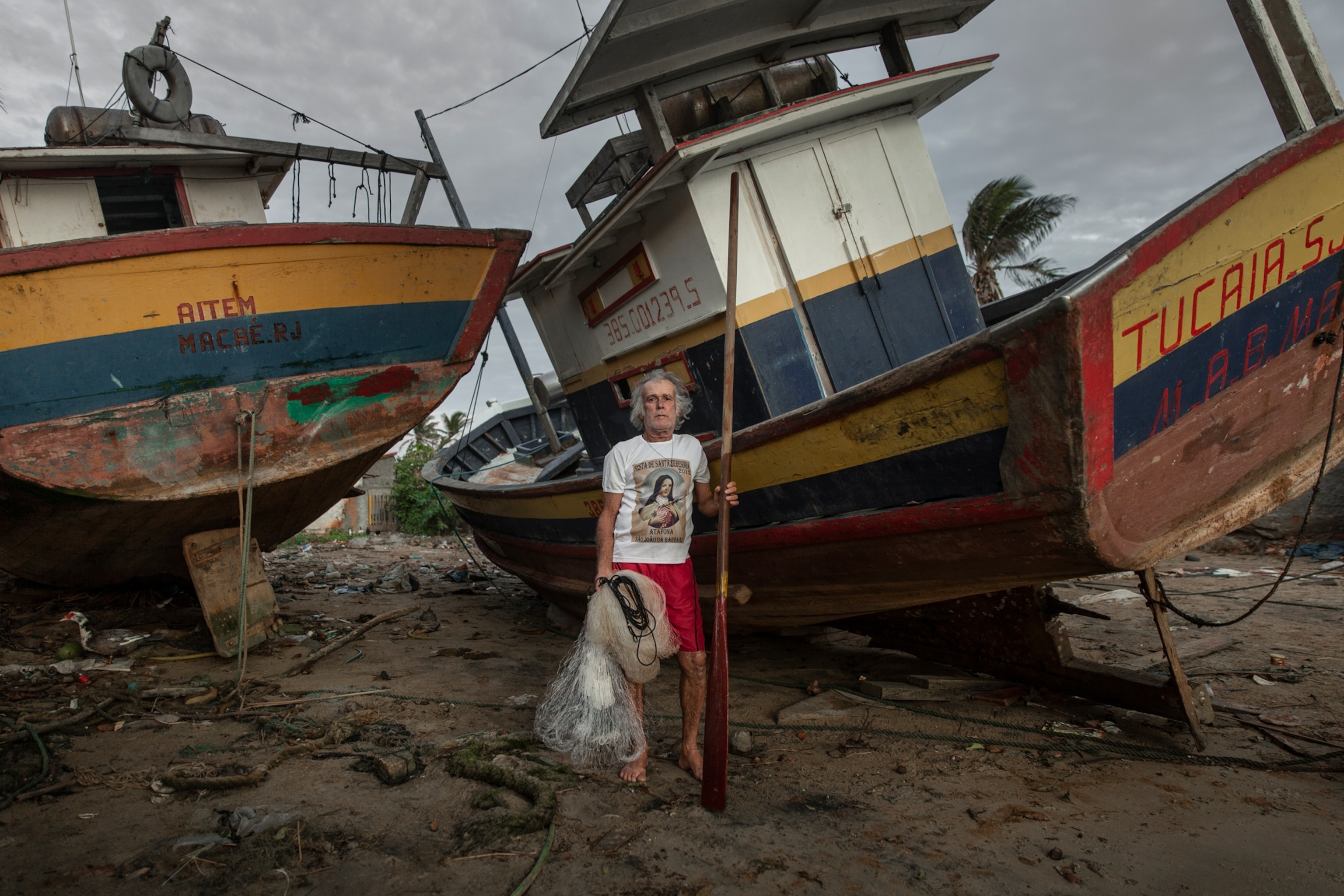 a fisherman stands in front of two boats on land holding a net