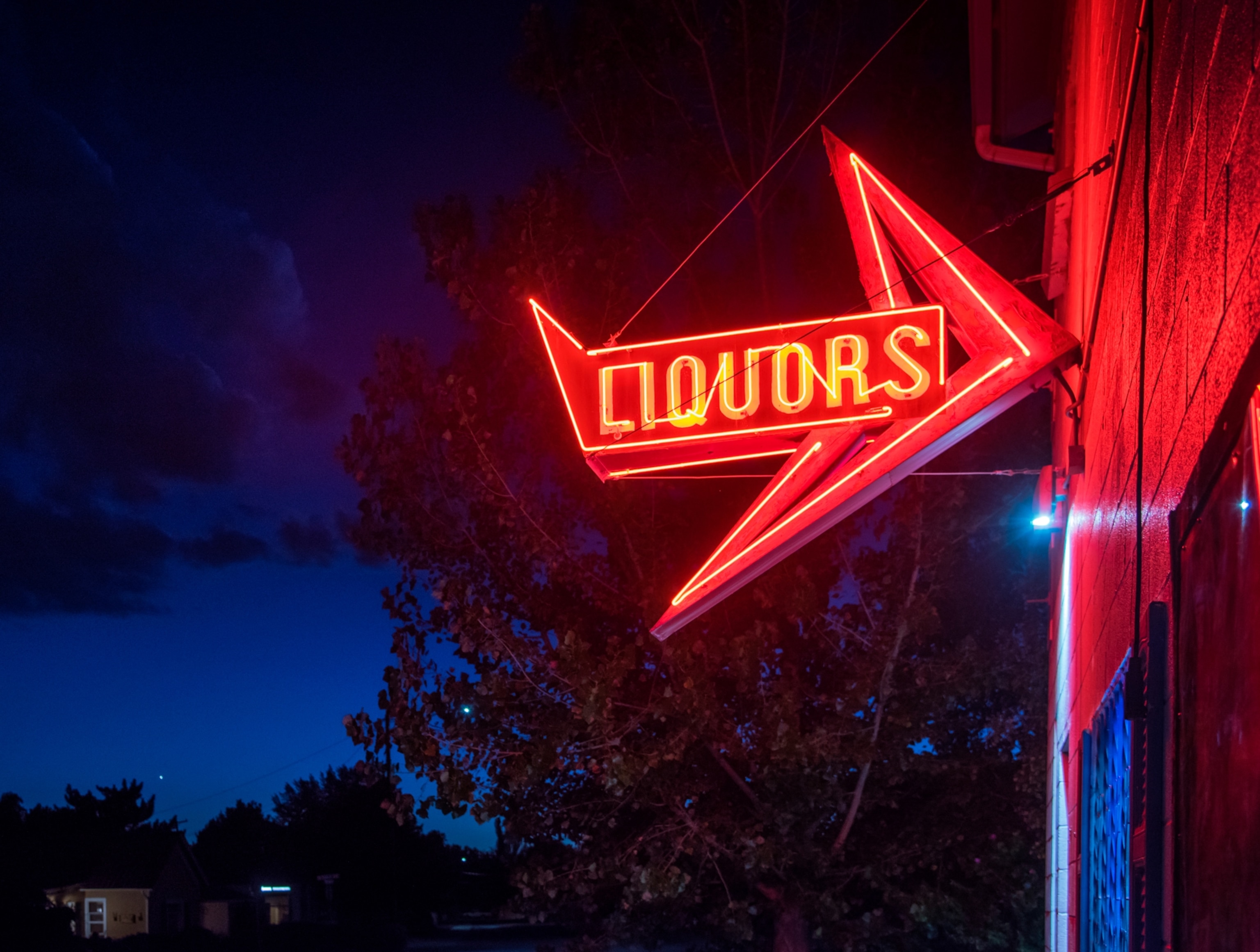 A red neon "liquor" sign against a blue sky at dusk.
