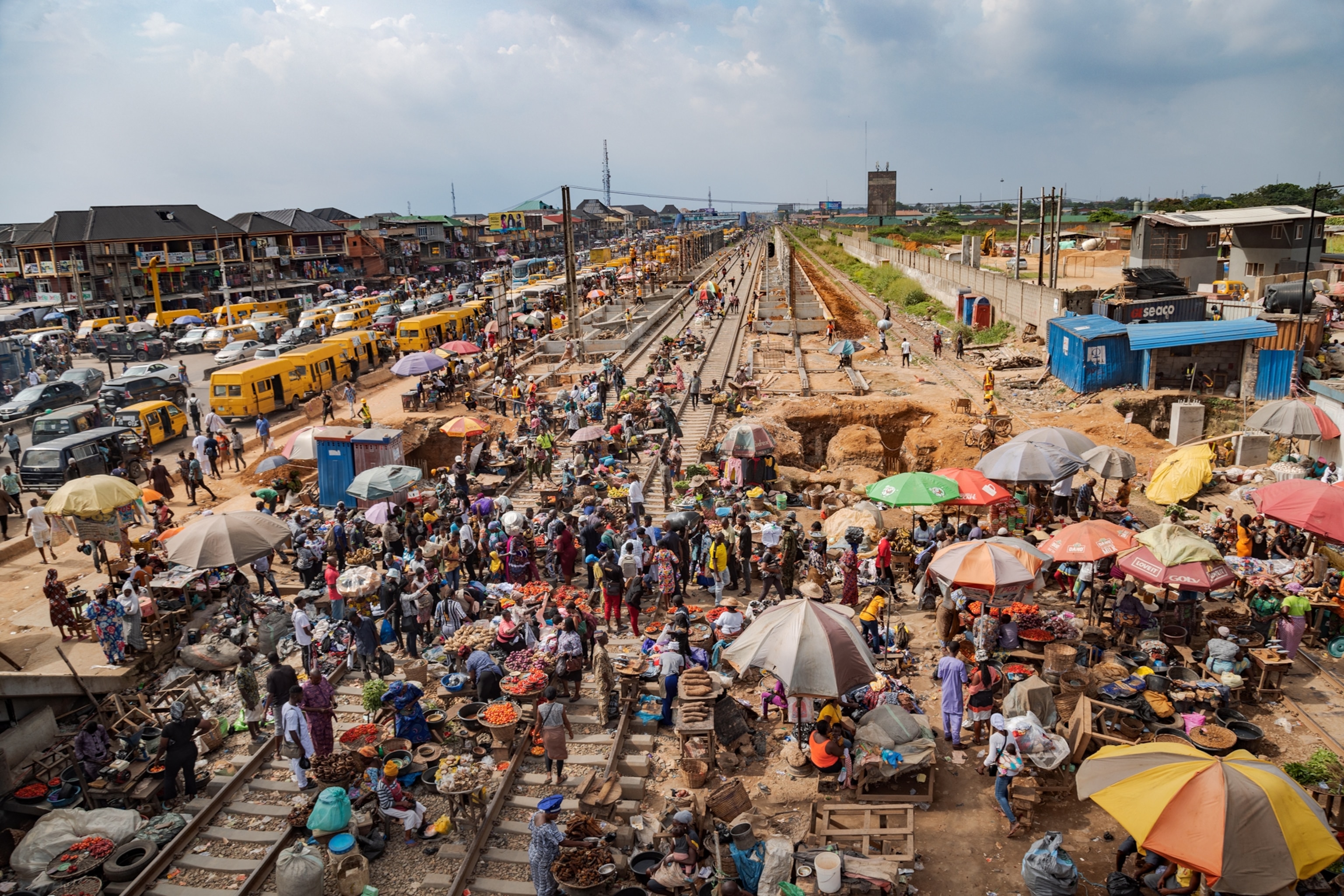 Picture of busy market on railroad tracks with yellow buses lined up along them.