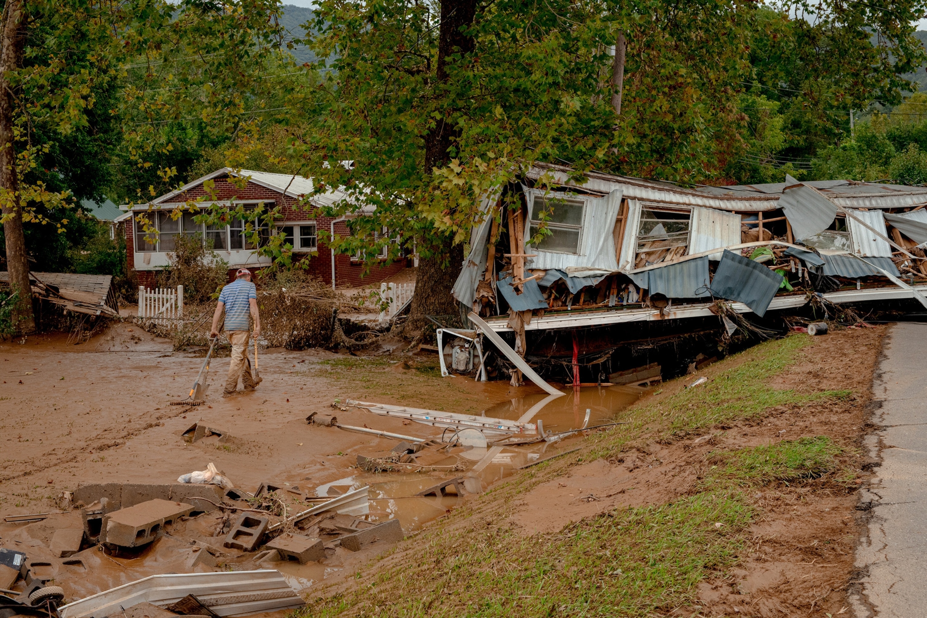 A man walks through mud towards a destroyed house along the Swannanoa River in Swannanoa, N.C.