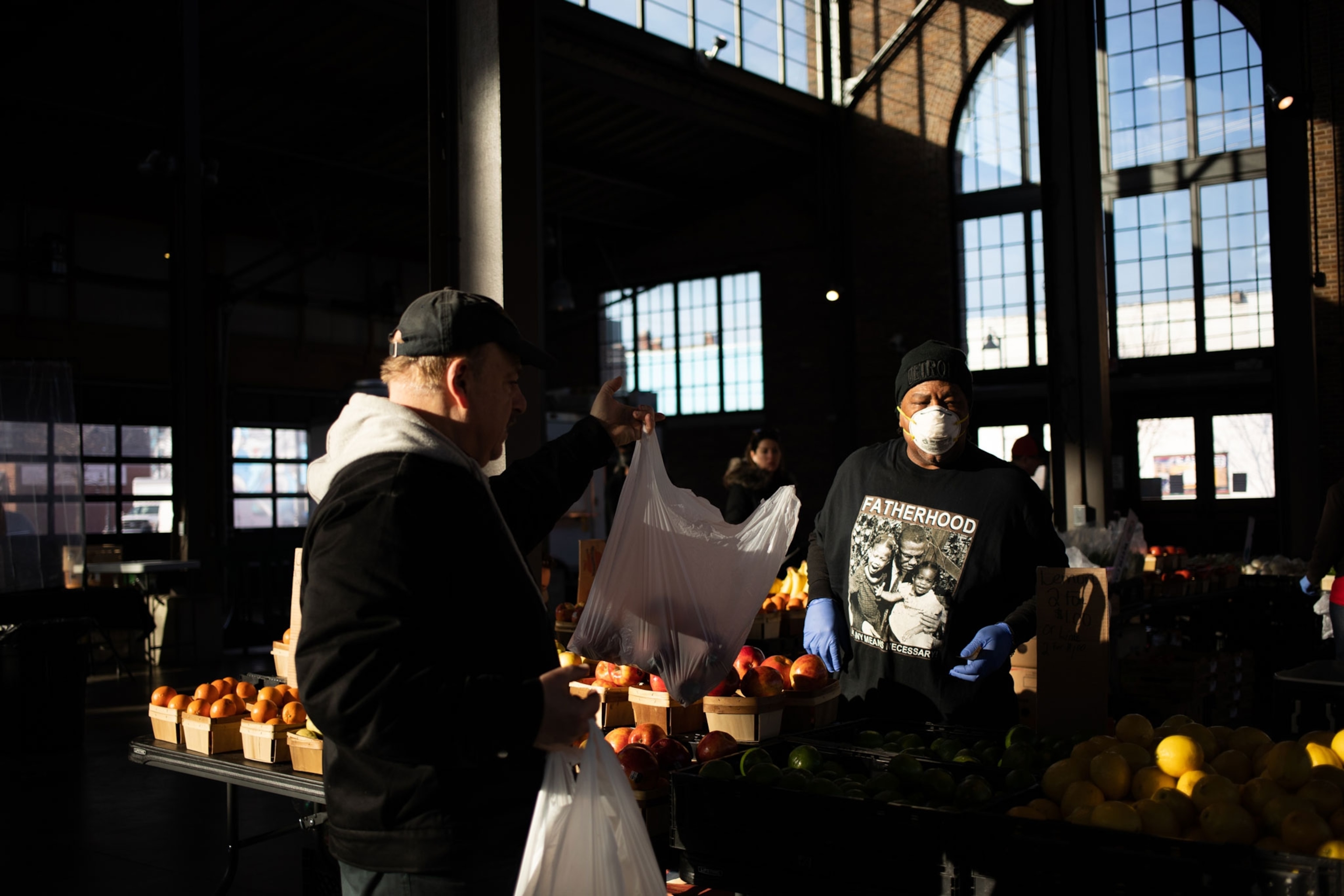 a man at a fruit stand wearing a mask and helping a customer