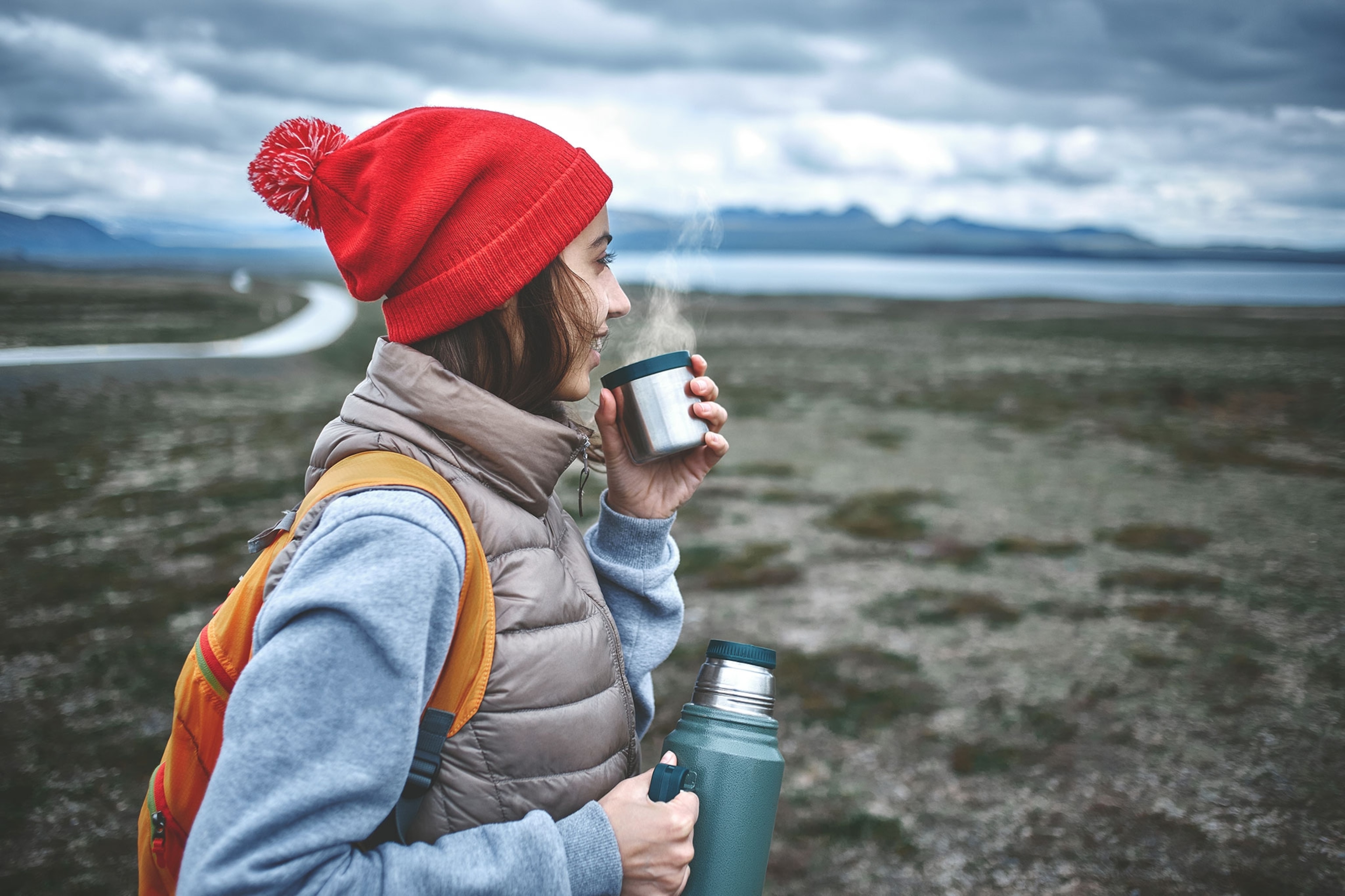 Woman wearing a red hat and holding a steaming cup of coffee outdoors.