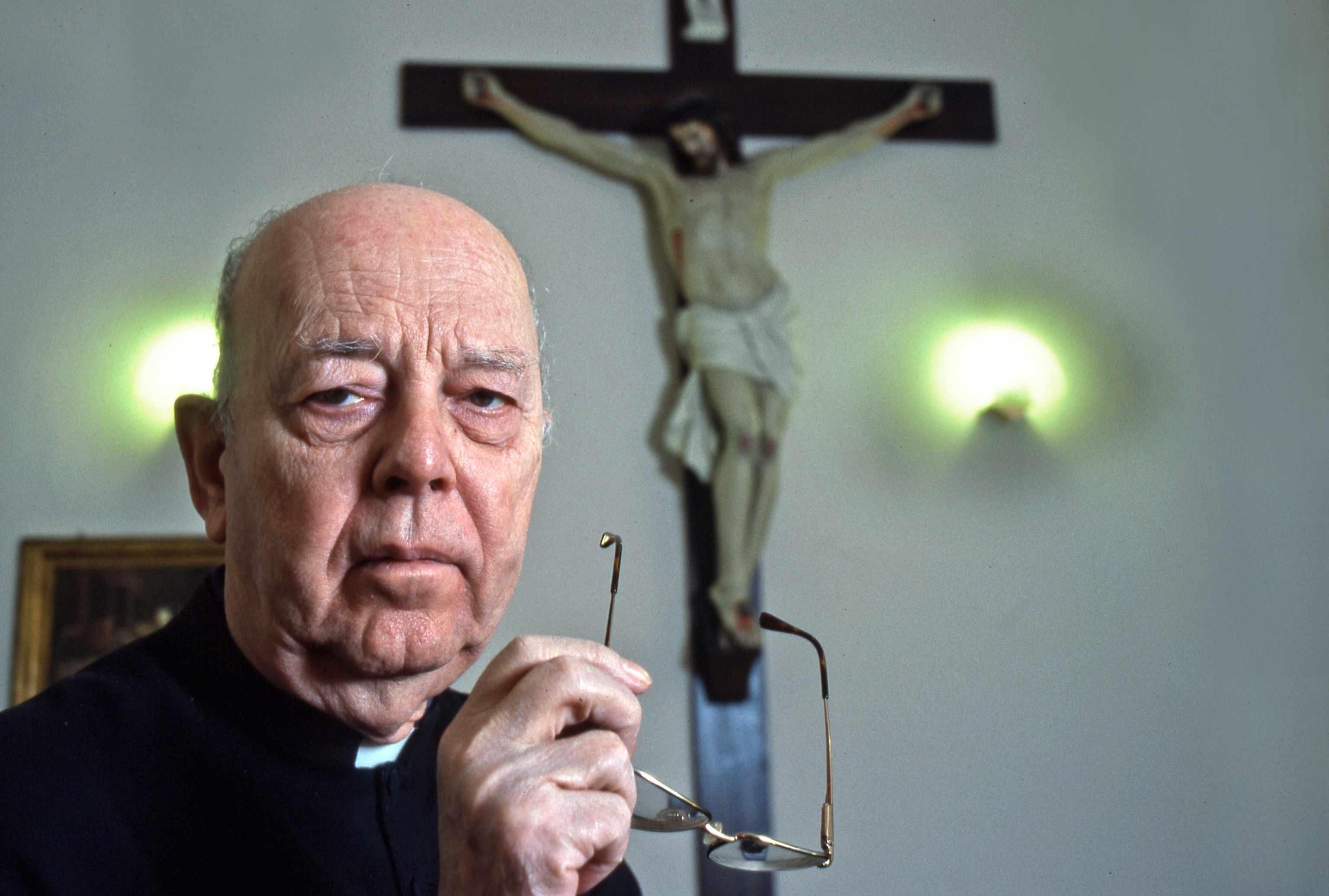 Photo of priest with crucifix behind him