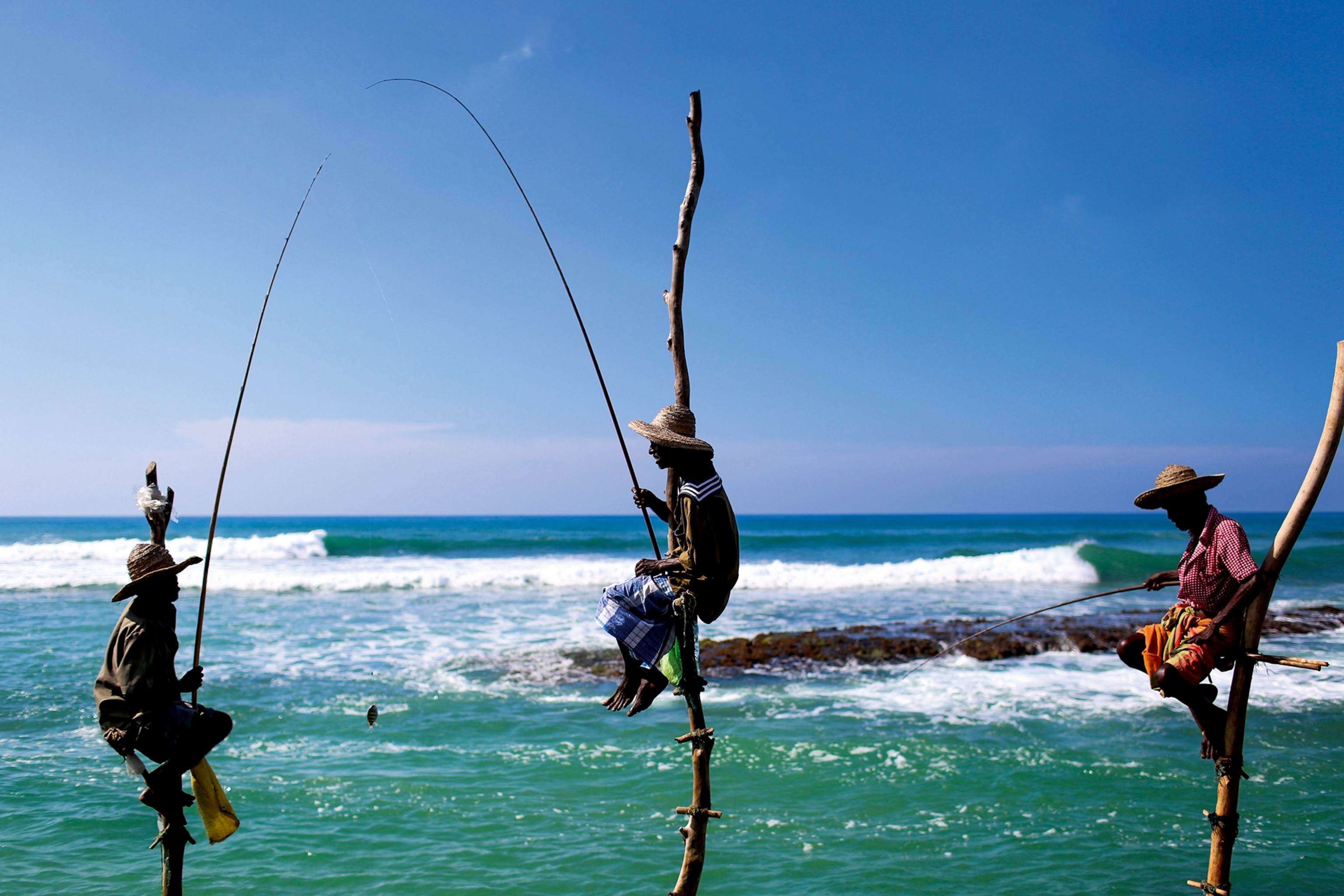 Men balancing on wooden poles overlooking the sea