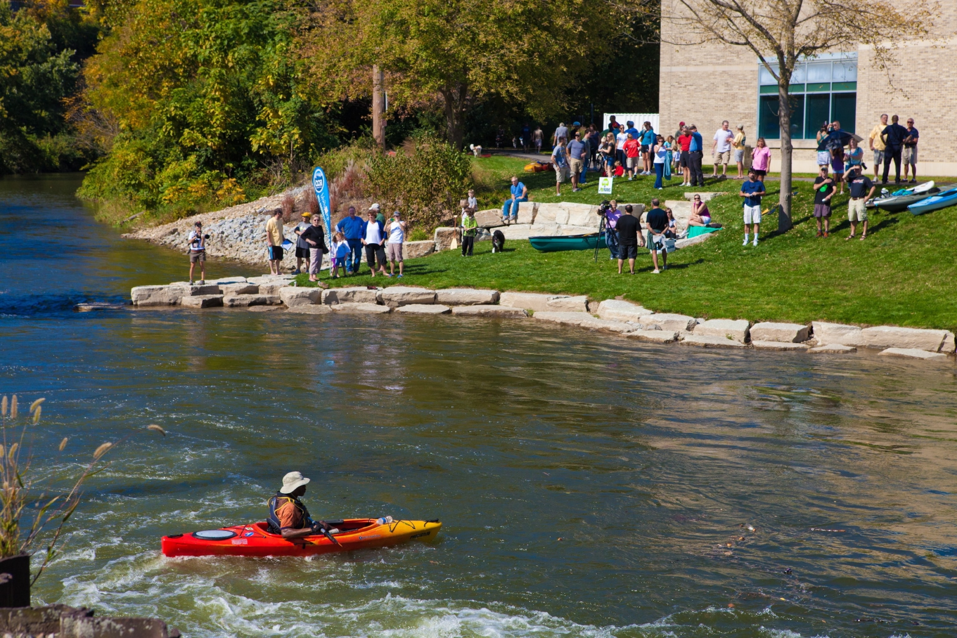 Many people looking at a creek while a man kayaks