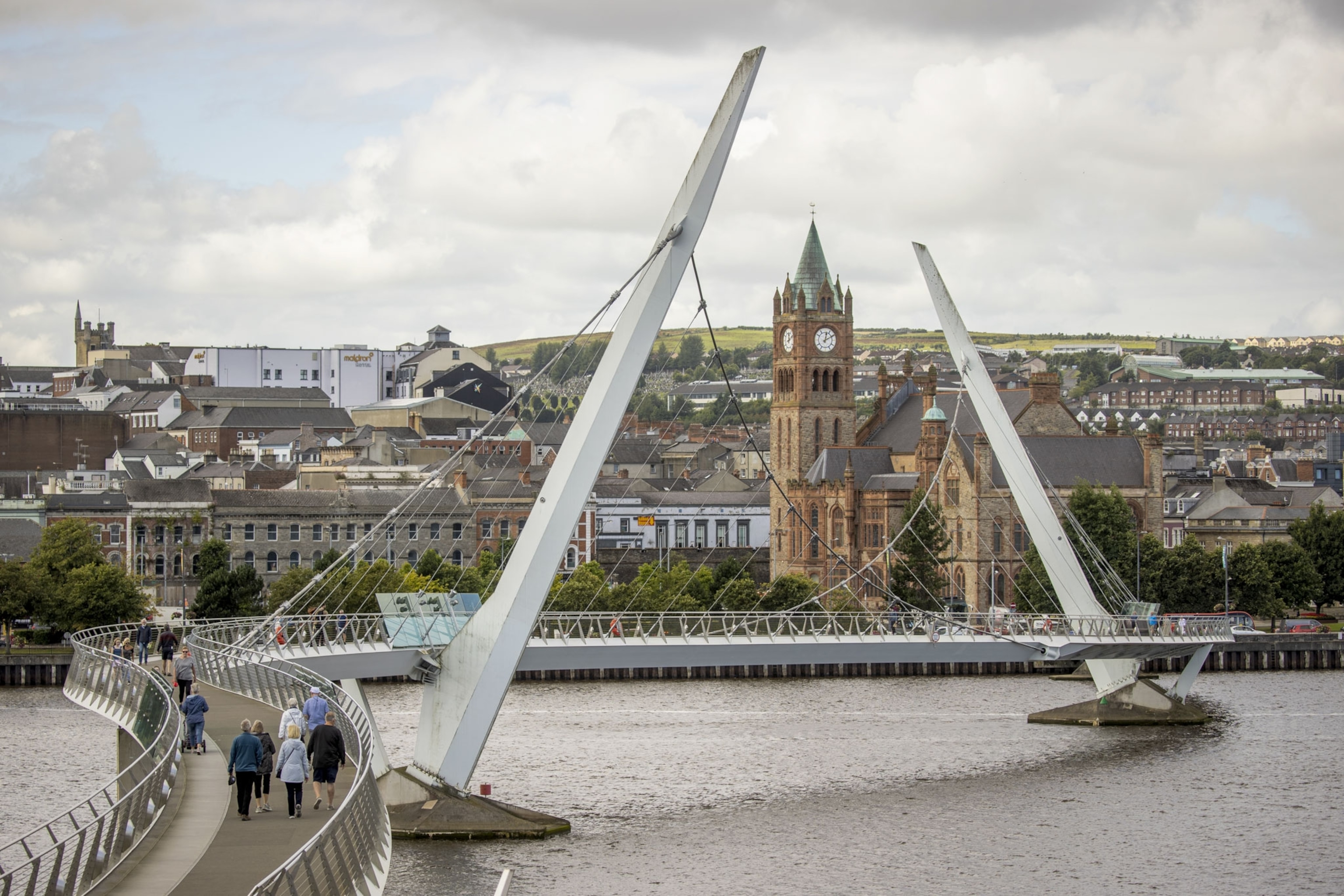 people walking across a suspension bridge called the peace bridge in Derry City, Ireland