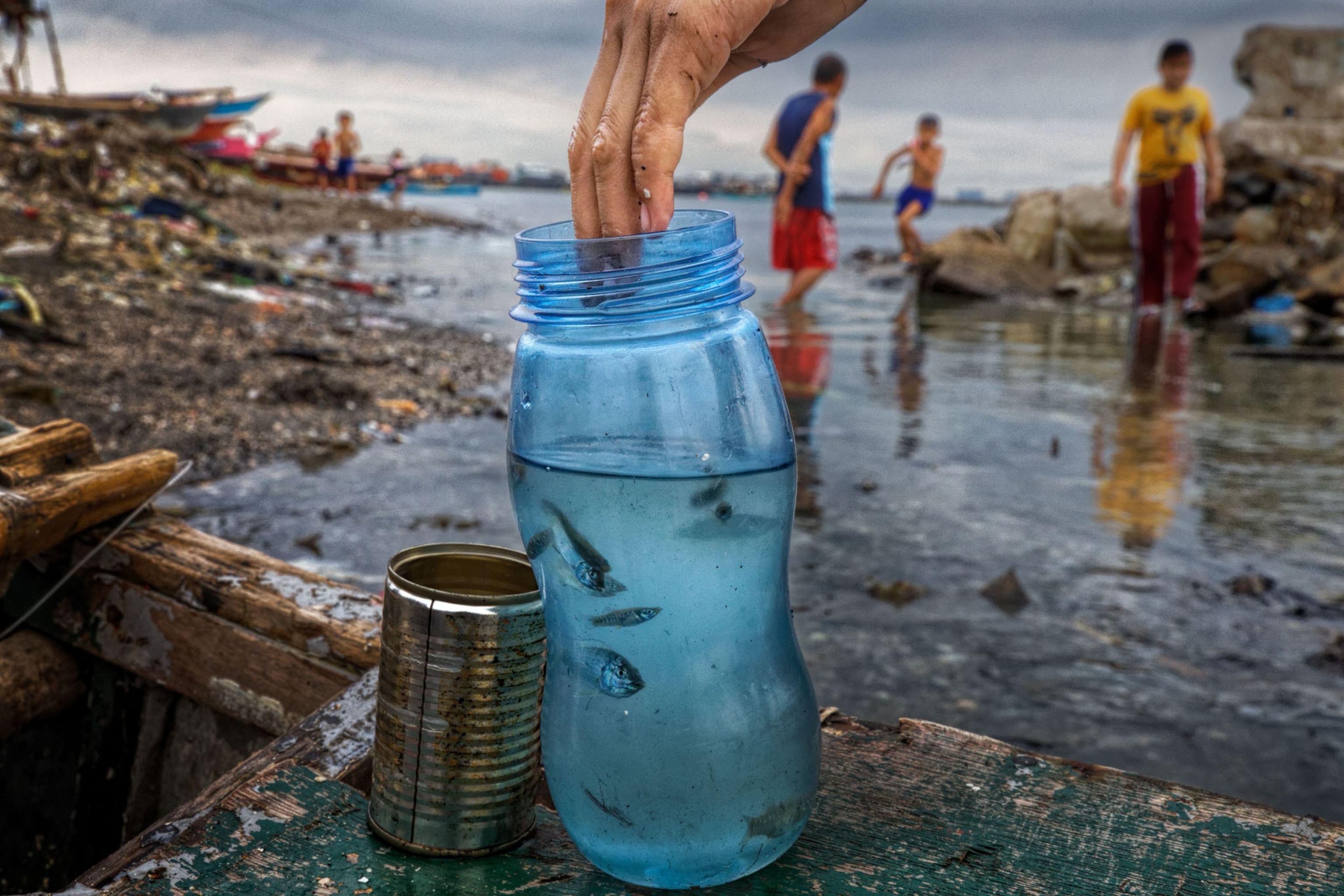 a plastic blue bottle filled with water and small fish, in the background a shore scene