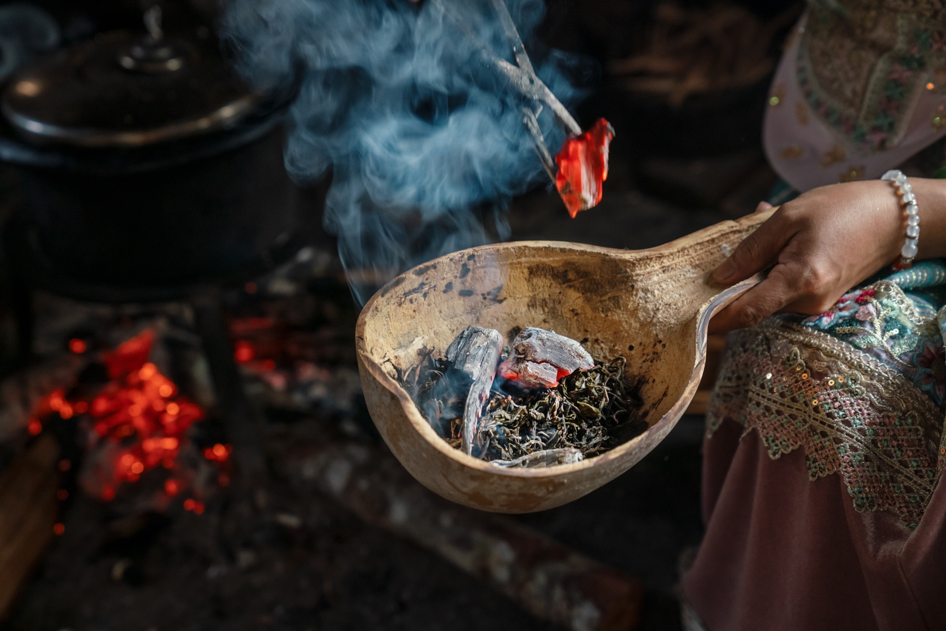 A woman infuses a bowl of tea leaves with smoke from burning wood.