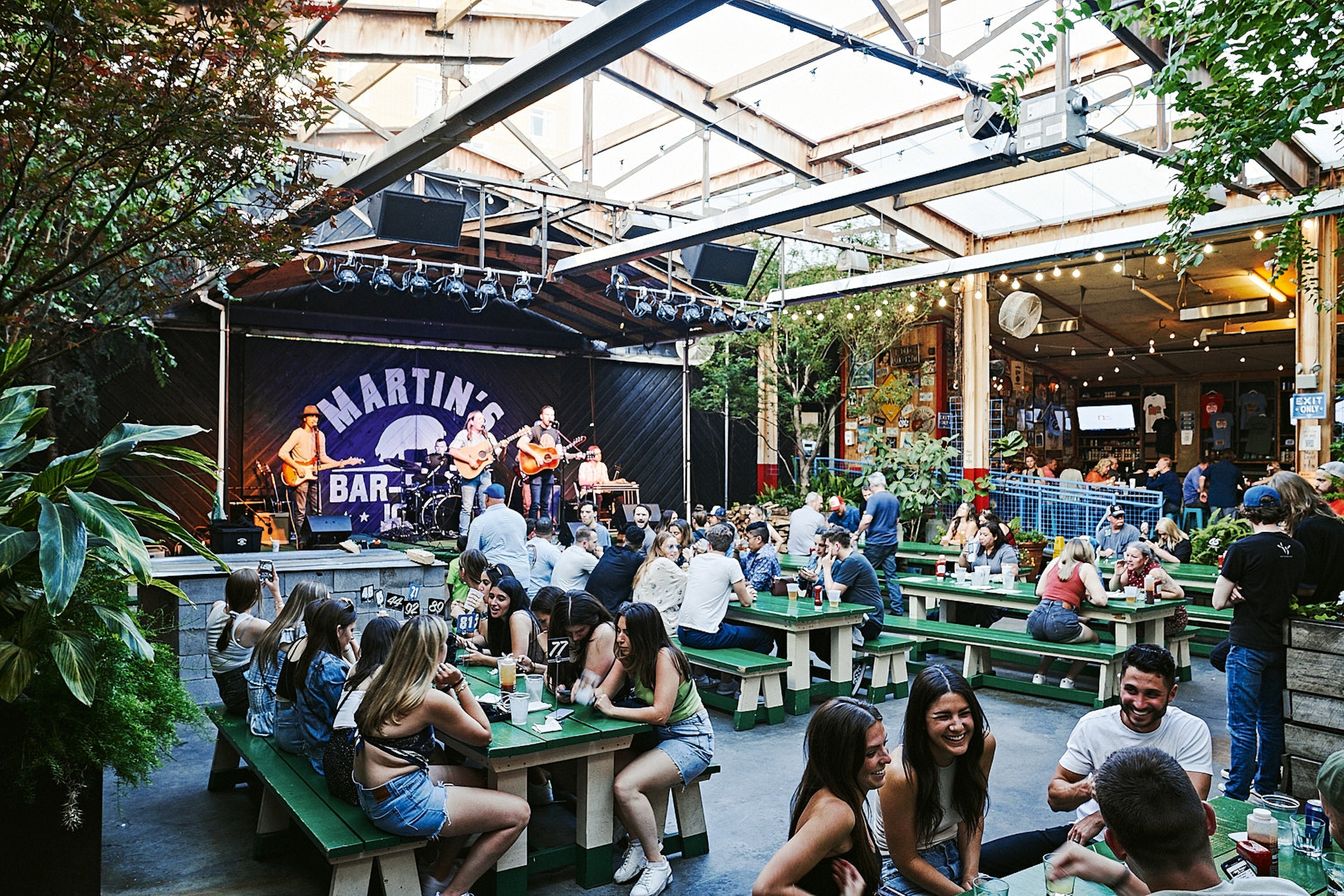 A busy winter-garden-style beer garden with a band playing on a stage in the back.