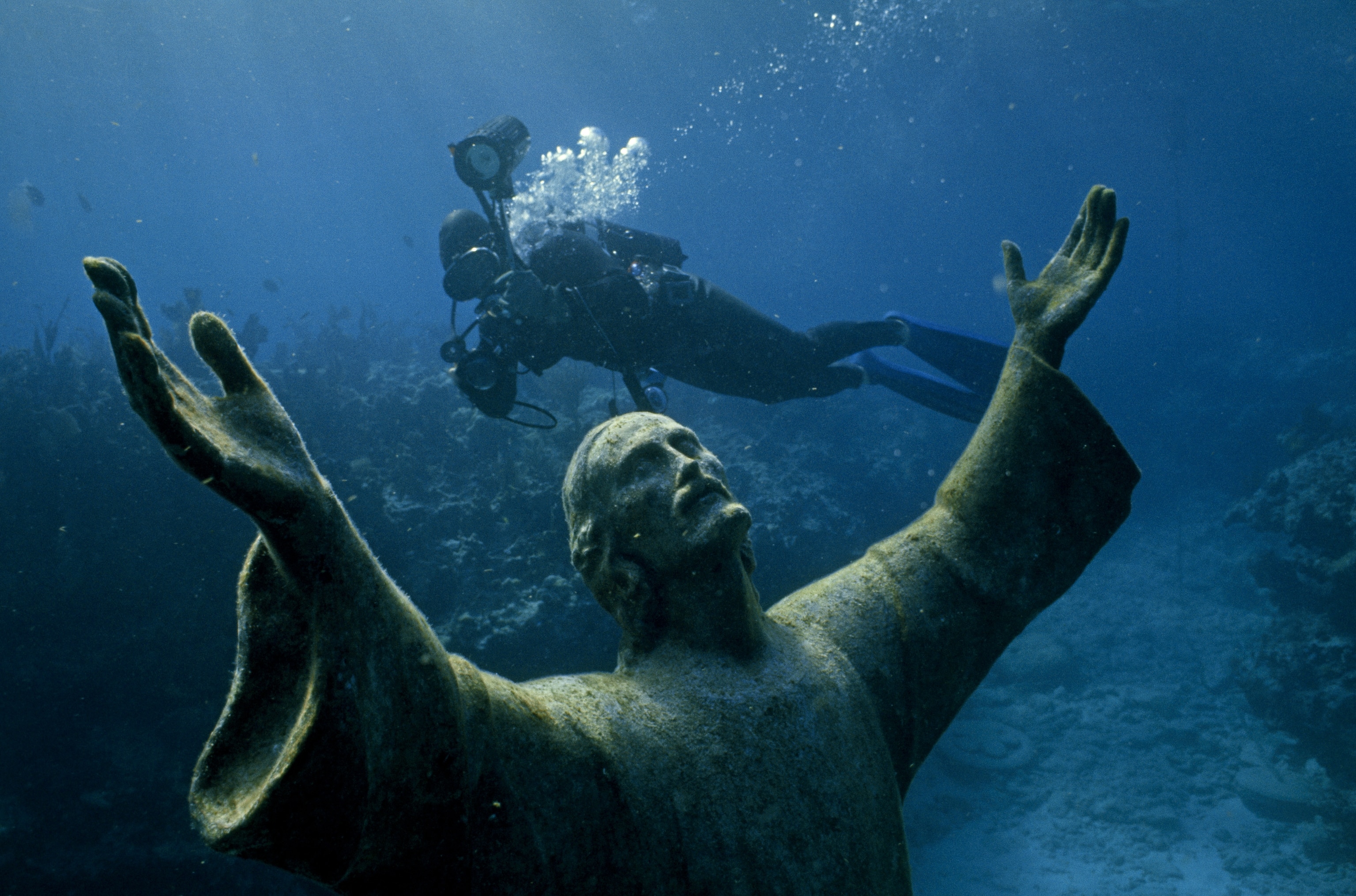 A scuba diver swims past the statue of Christ of the Abyss.