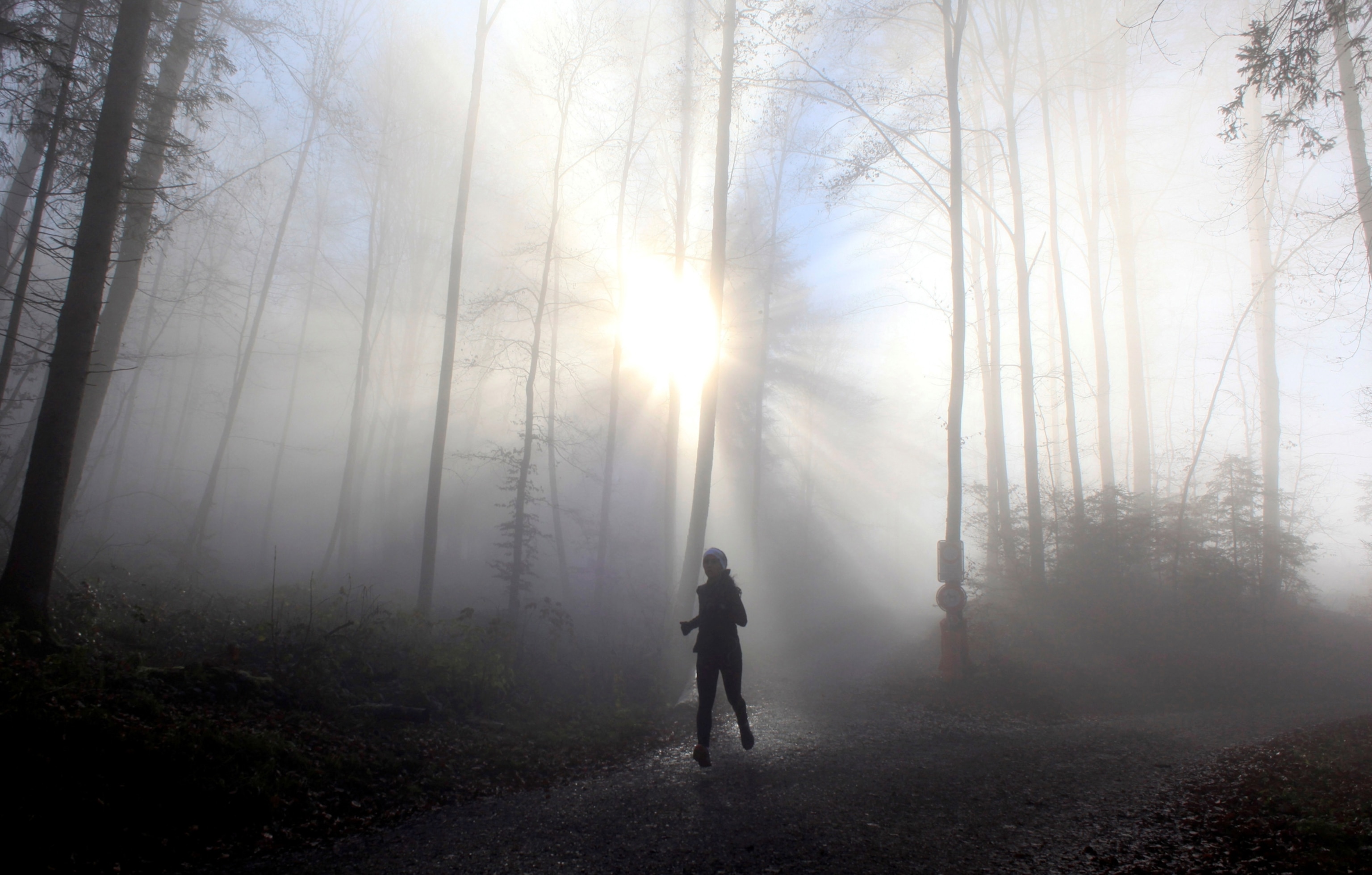 A woman jogging in a foggy forest as sun rays pierce through the fog.