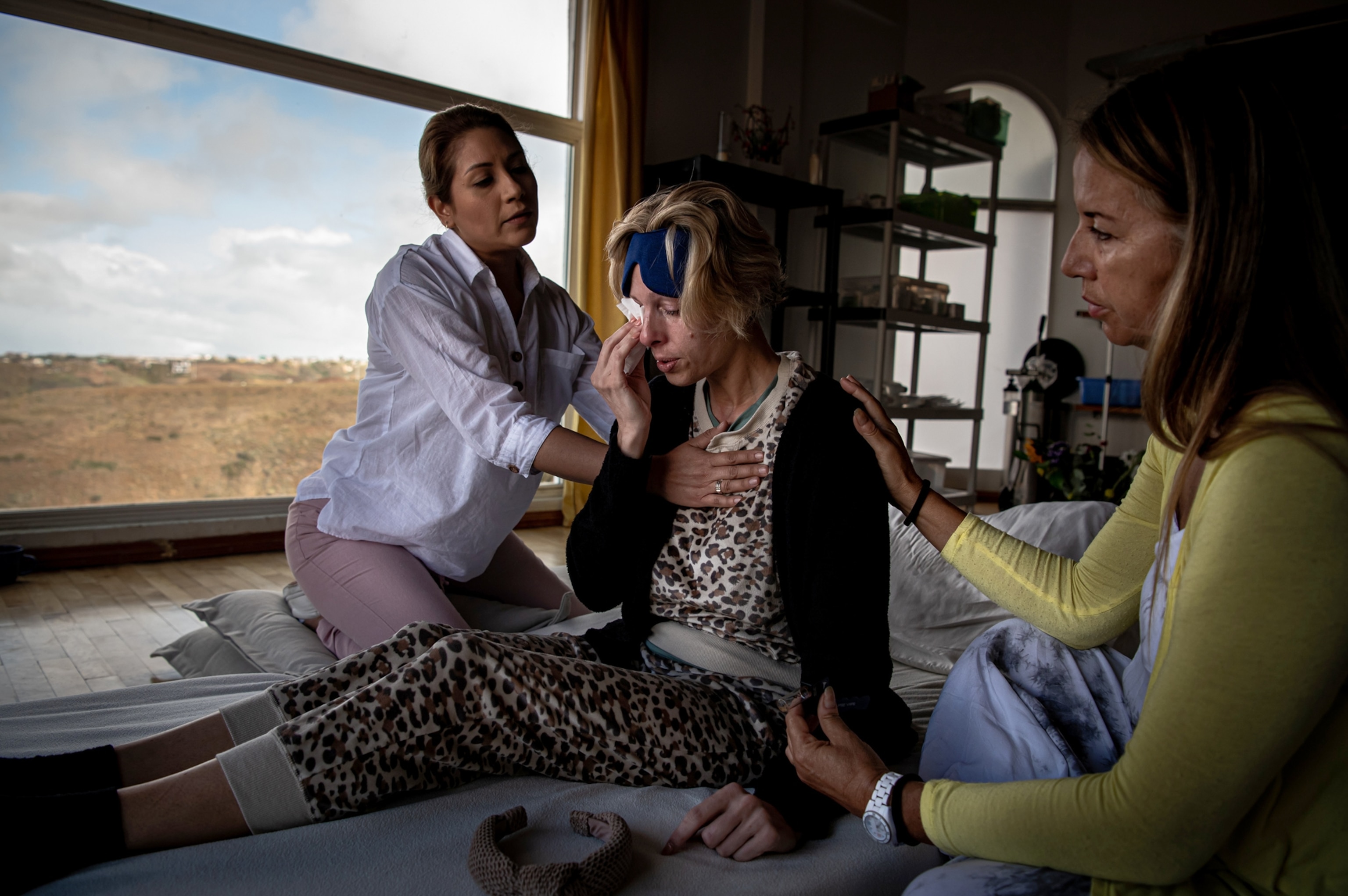 Two women gently touch and comfort a third woman who is wiping tears from her eyes after taking DMT.