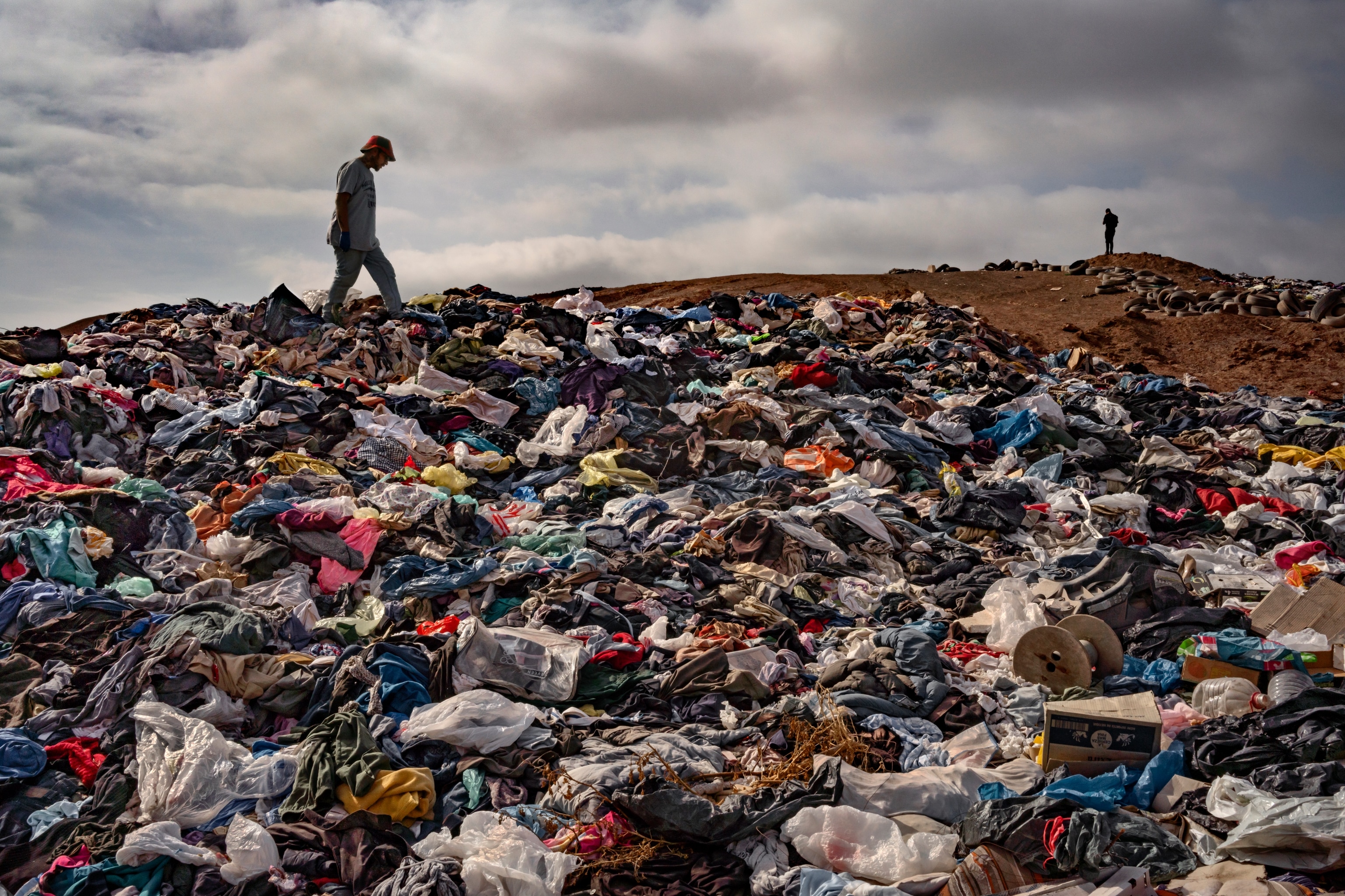 Man stepping on top of a mountain of dumped clothes