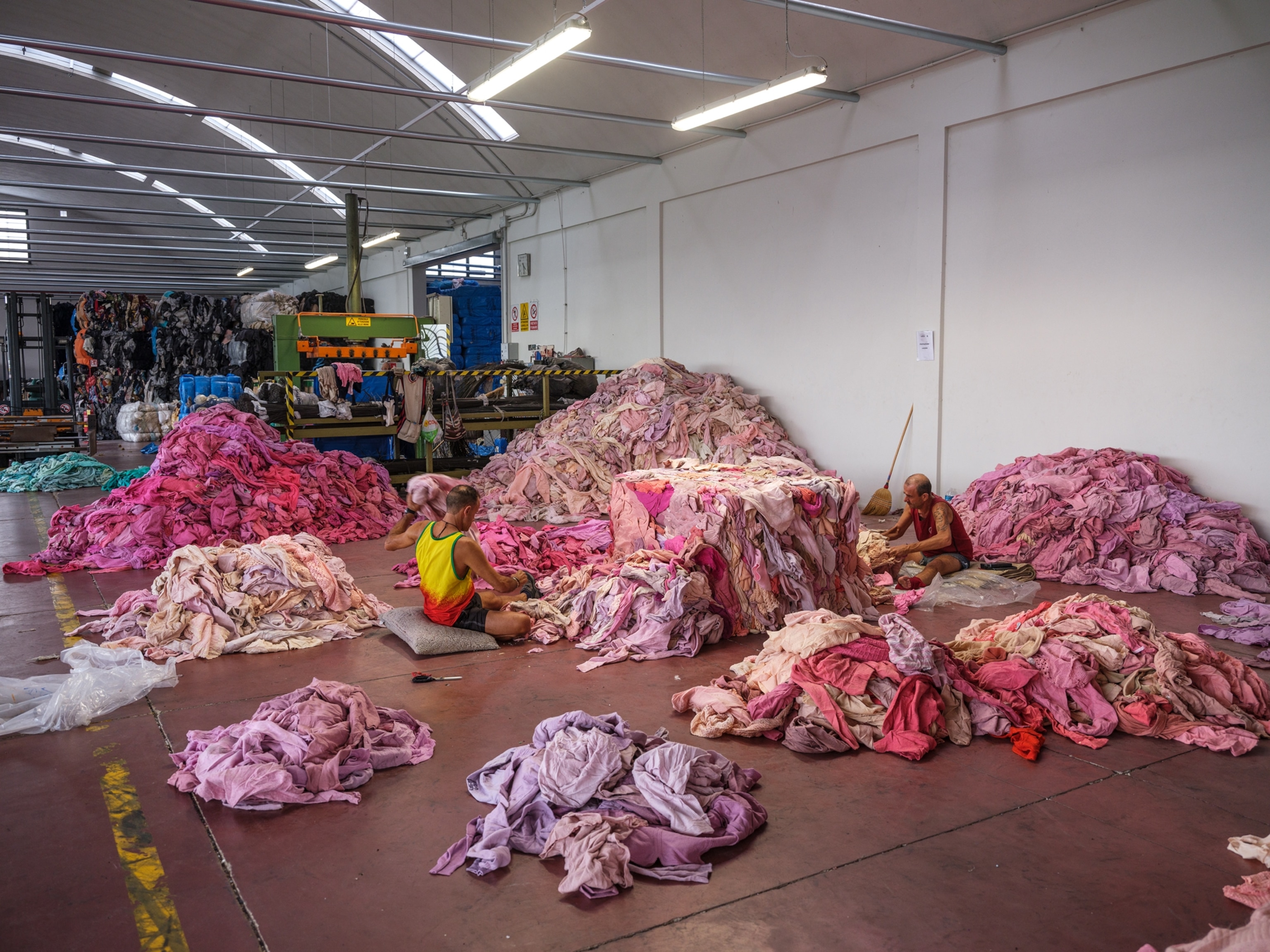 Two men sorting through large piles of pink and purple clothing