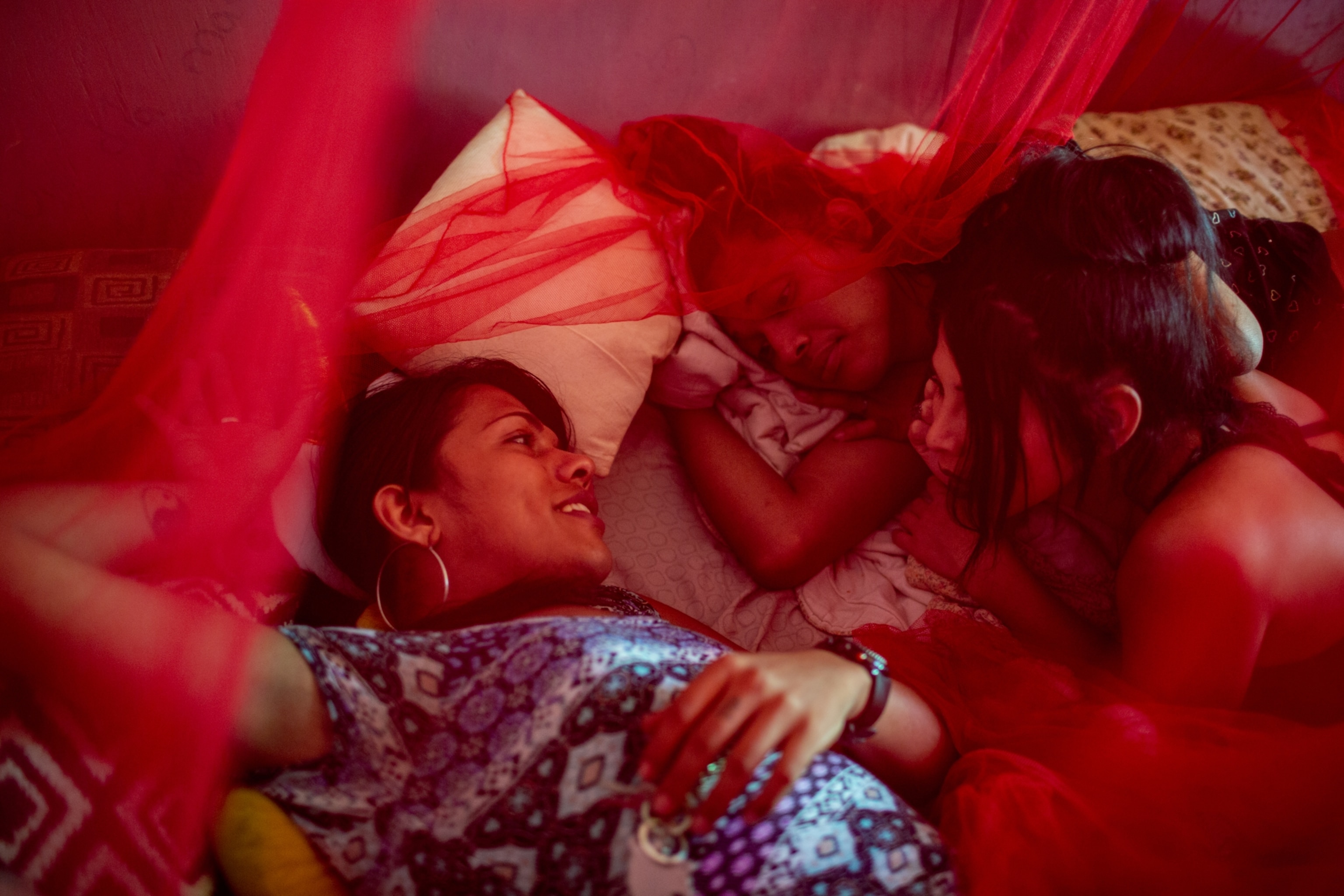 three people lying underneath a red mosquito net