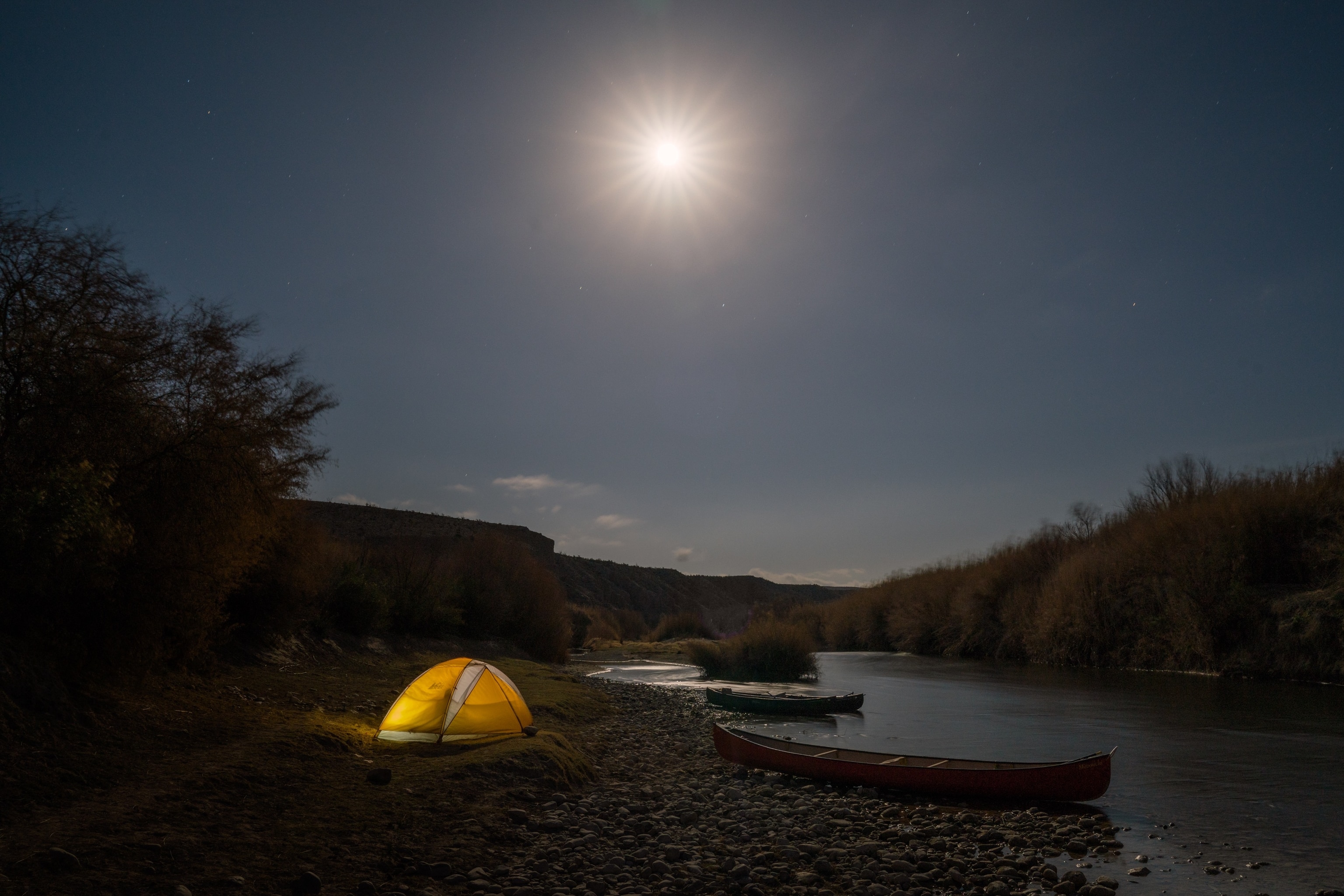 A bright moon shines above a tent and canoes camped along the river's edge of the Rio Grande near Boquillas Canyon and La Linda.