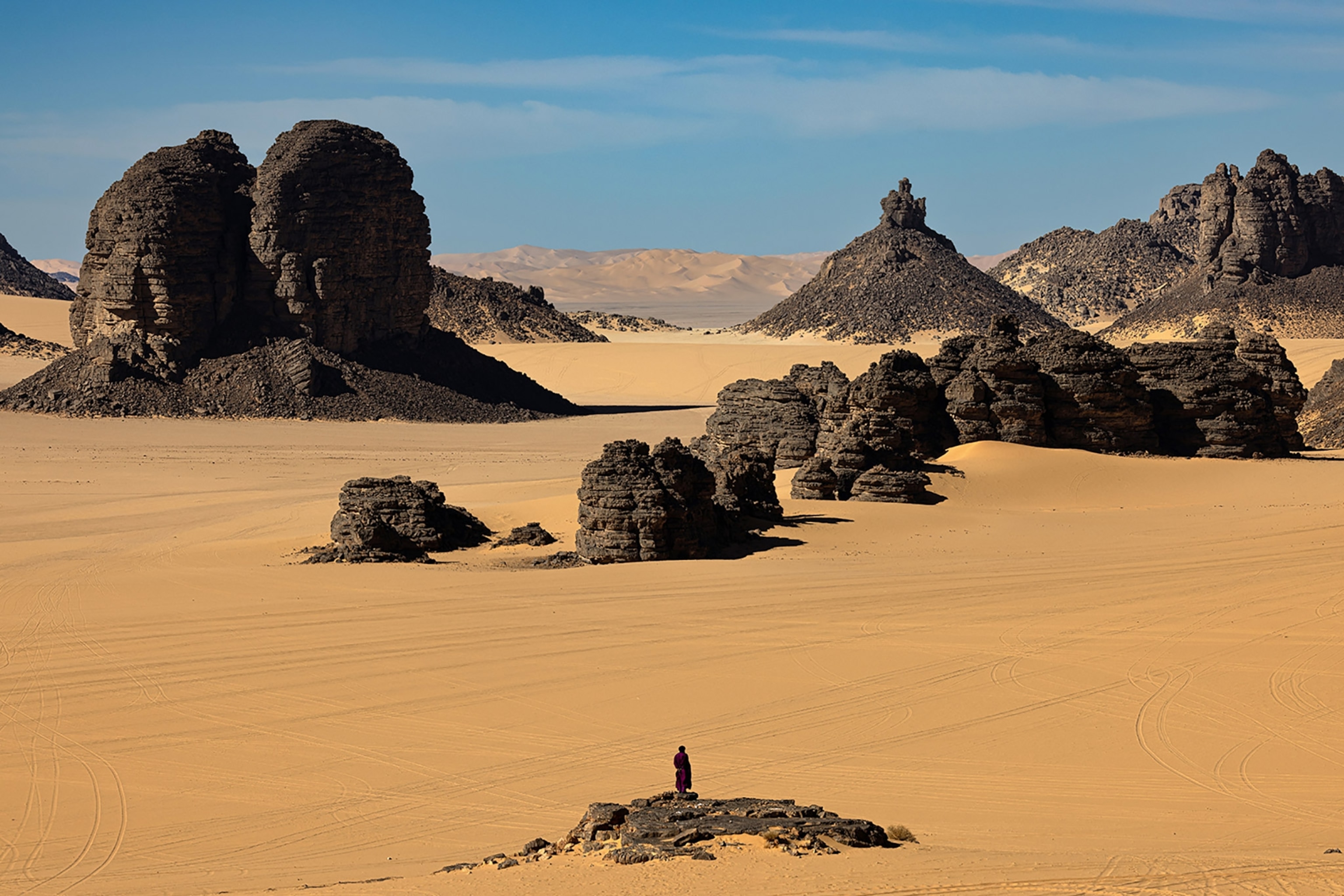 A guide, wearing the traditional robes and shesh headscarf of the nomadic Tuareg tribe, stands on an outcrop at Adrit.