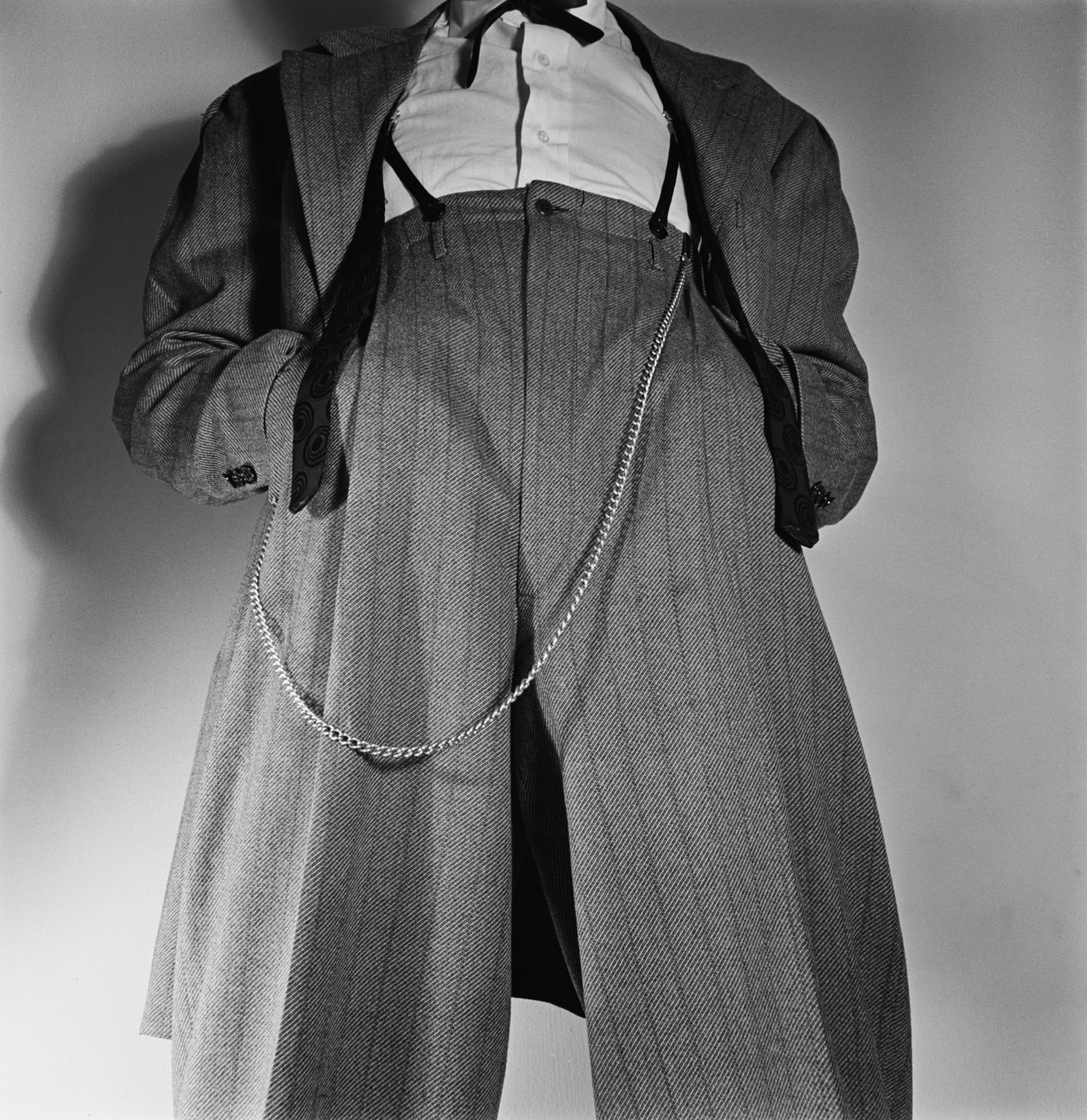 Low angle view of an unspecified man wearing a Zoot suit with a watch chain hanging from the waist, his hands in his pockets.