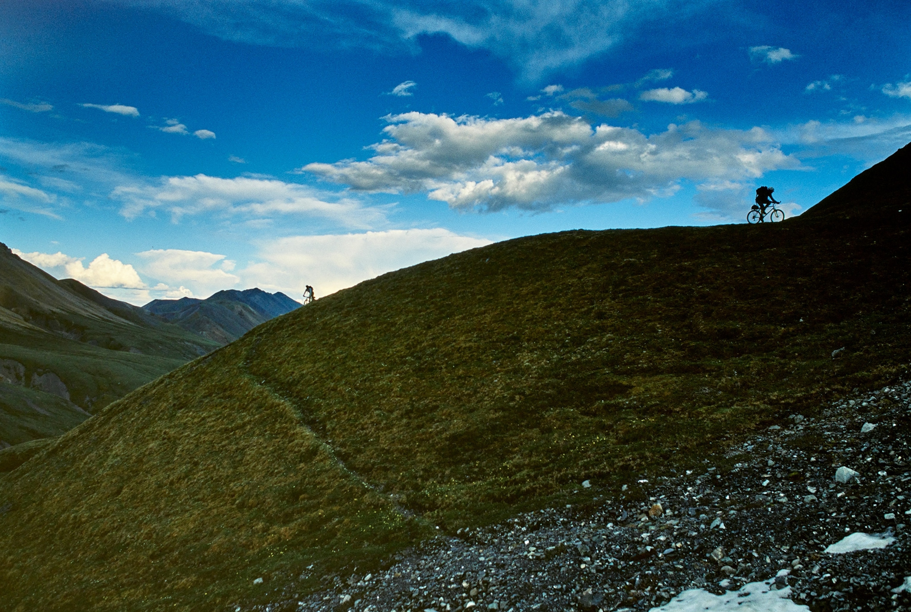Bikers cross the rough terrain and melted ice of southern Alaska's Range Mountains