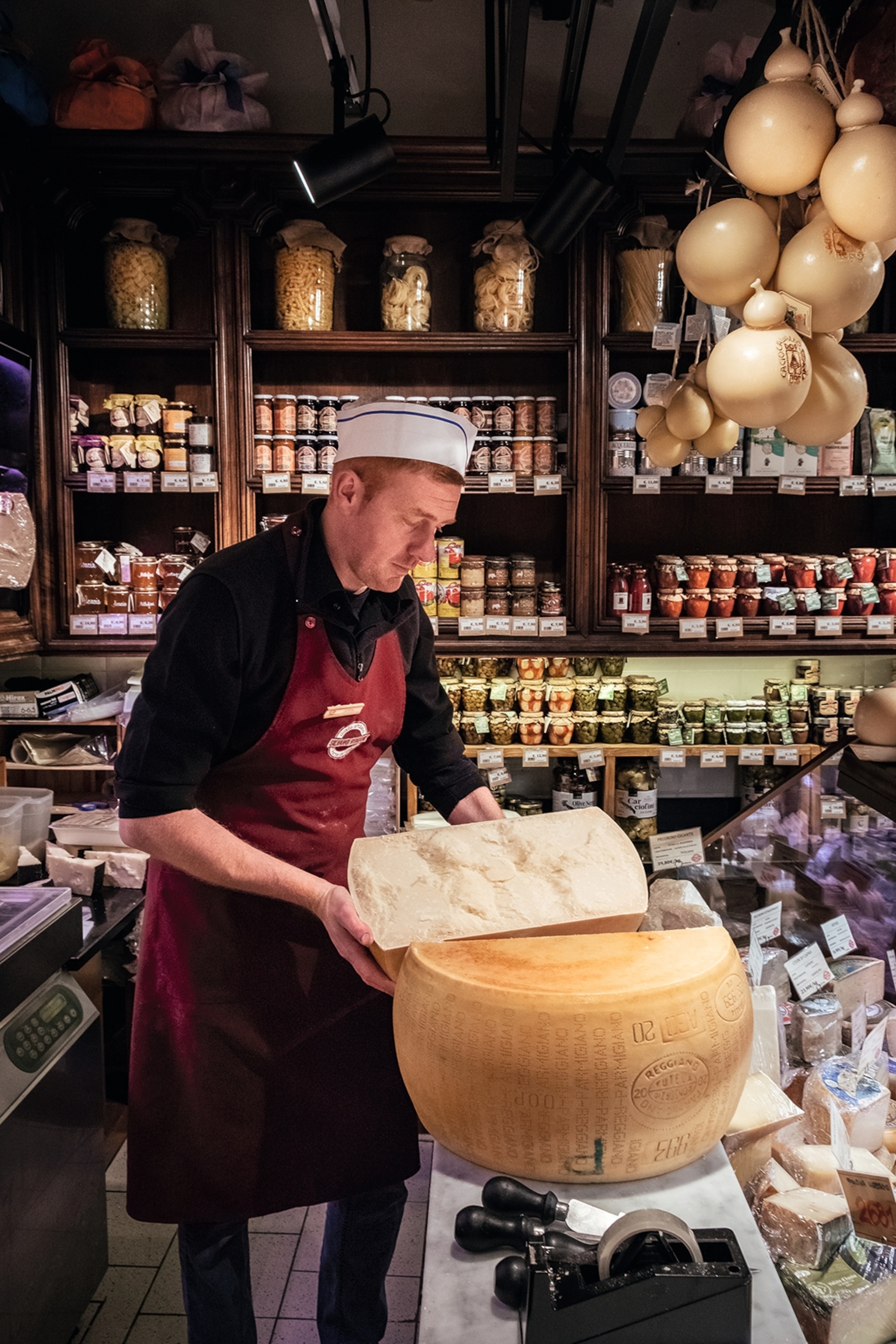 Luca opening a giant wheel of Parmesan behind the counter at La Prosciutteria.