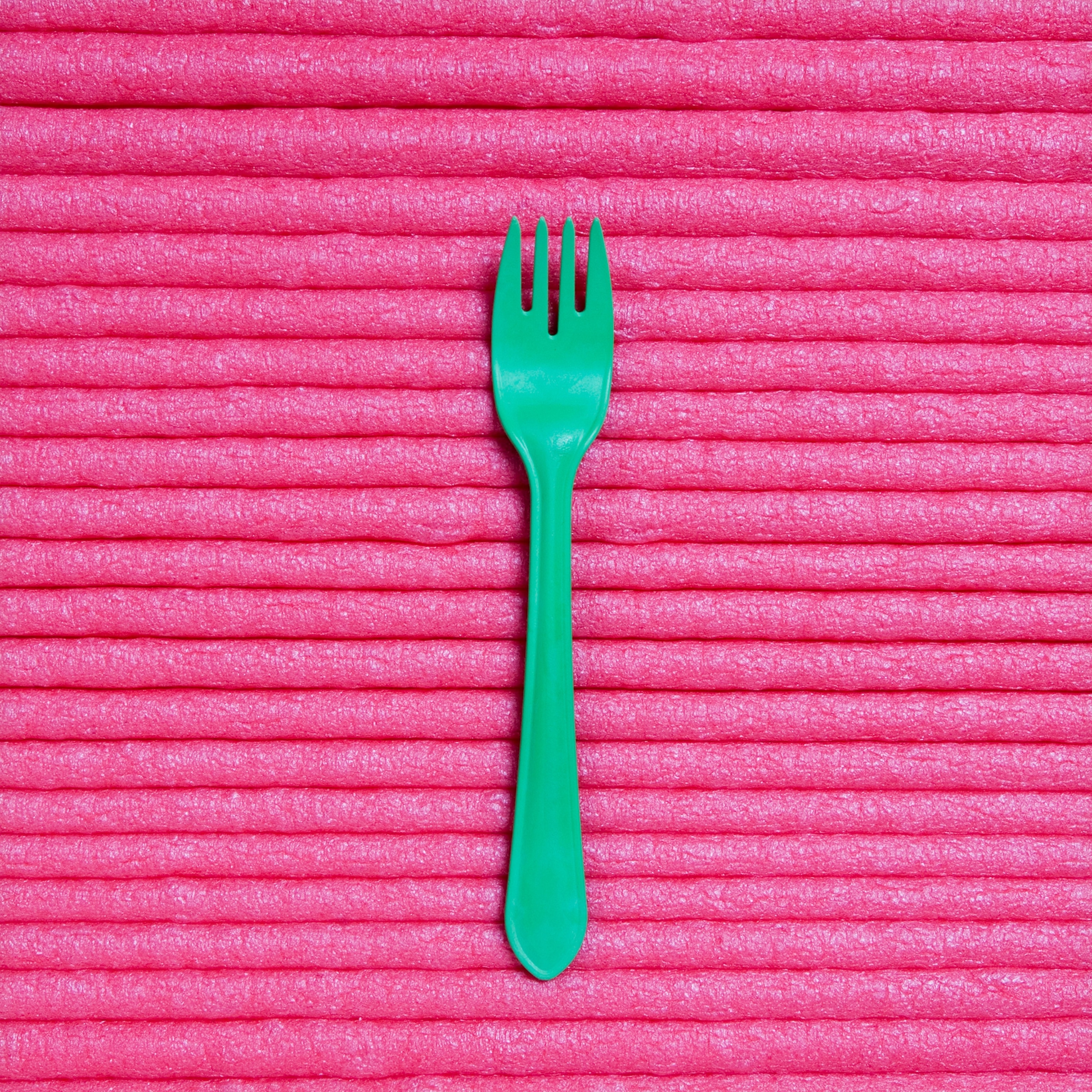 Still life of a green biodegradable plastic fork against a pink background.