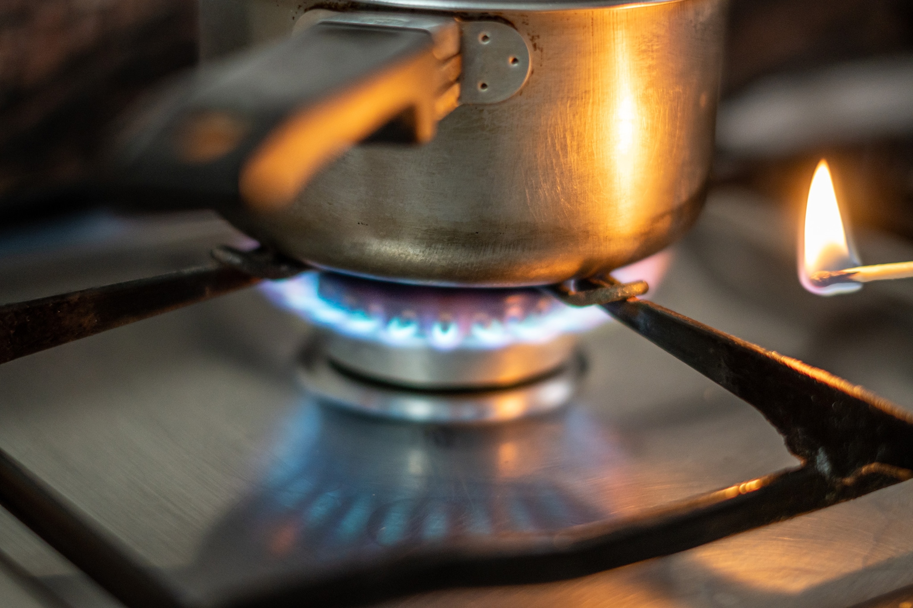 Saucepan on top of stove with burner on and lit match