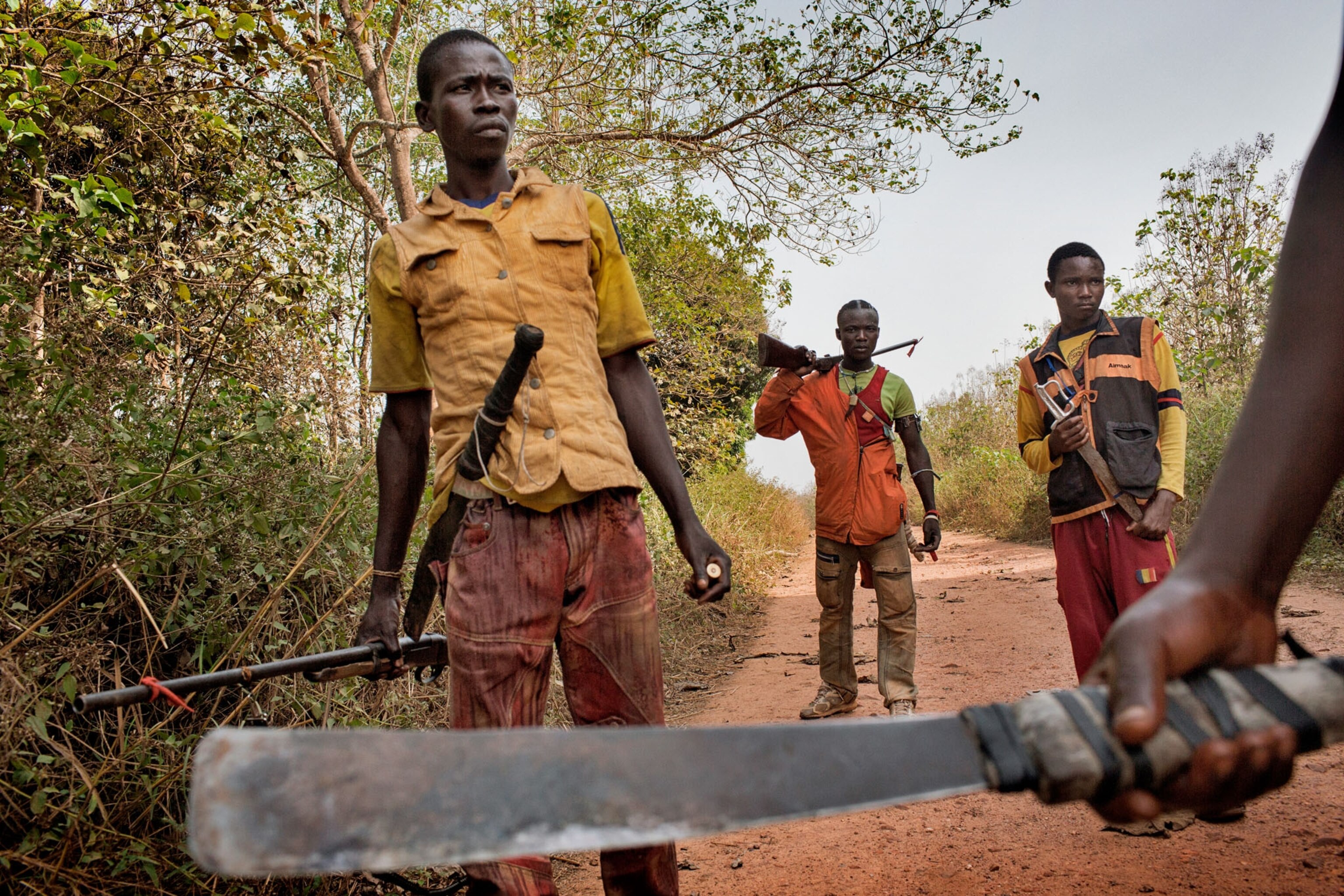 a group of young men from the anti balaka militia walking down a dirt road with weapons