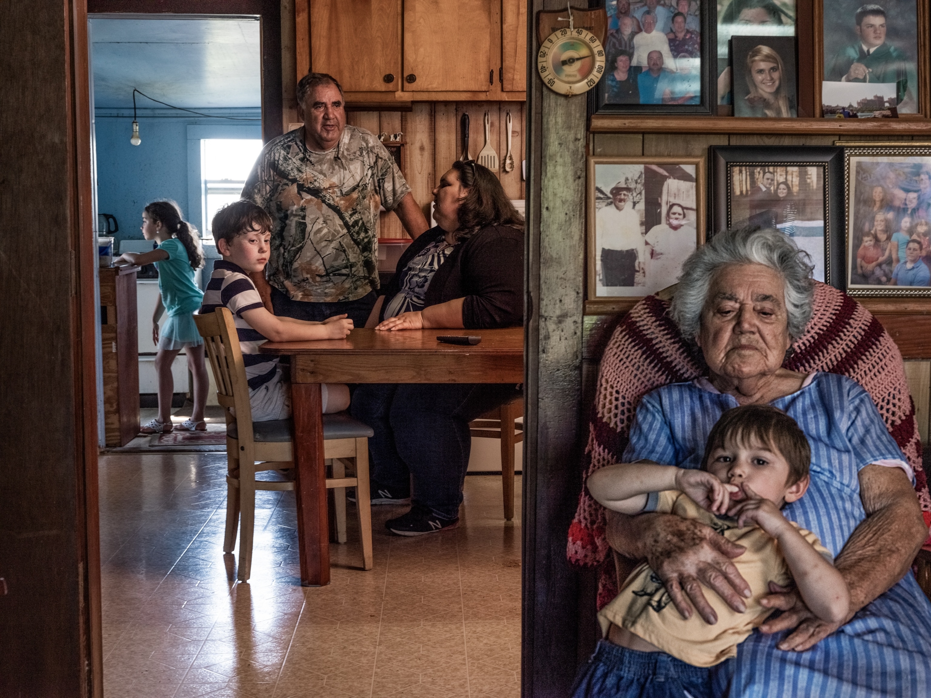 older woman with small boy sitting in armchair and her family on background.