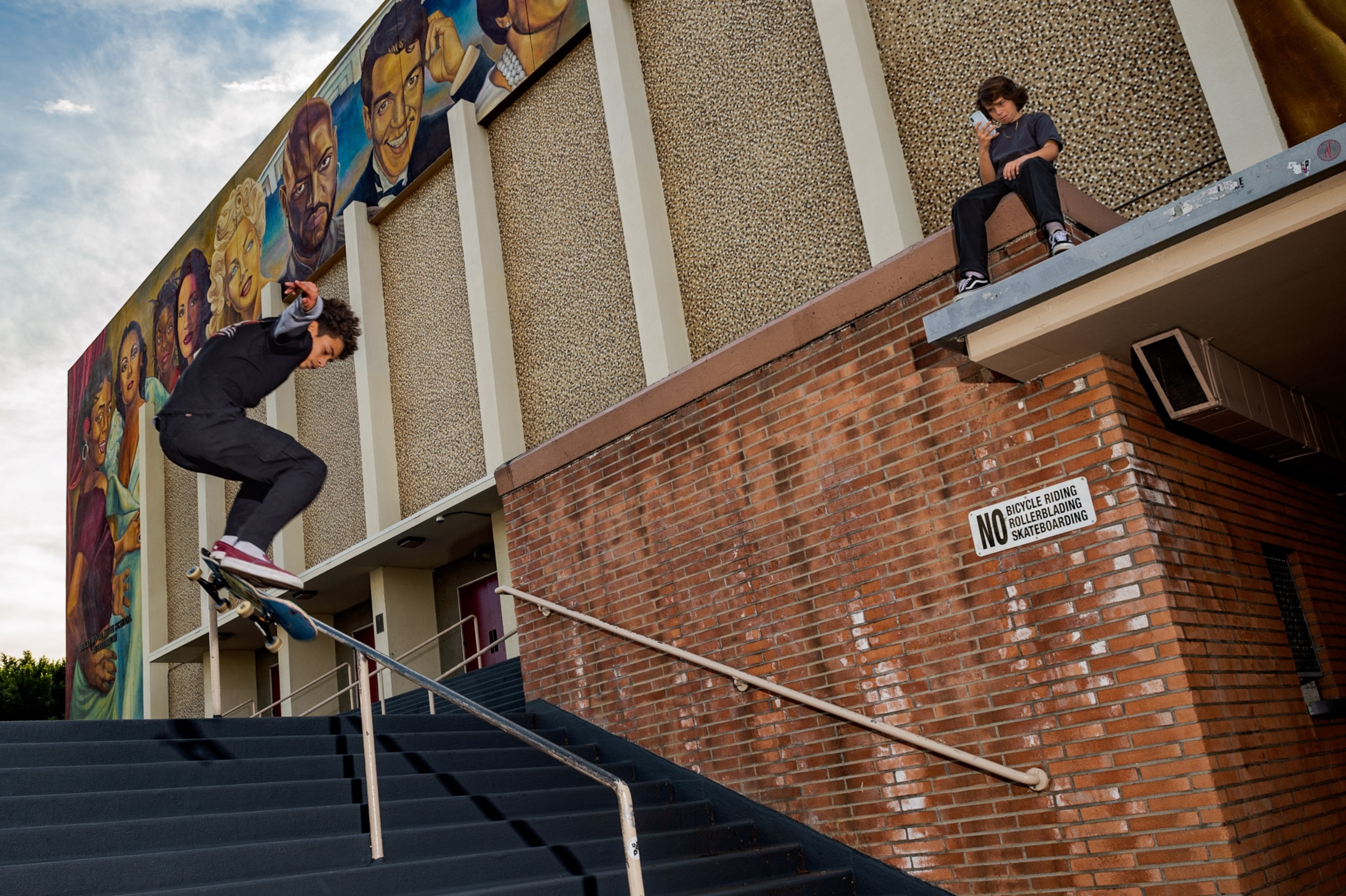 a boy skating down the railing of a set of stairs, while another watches from above